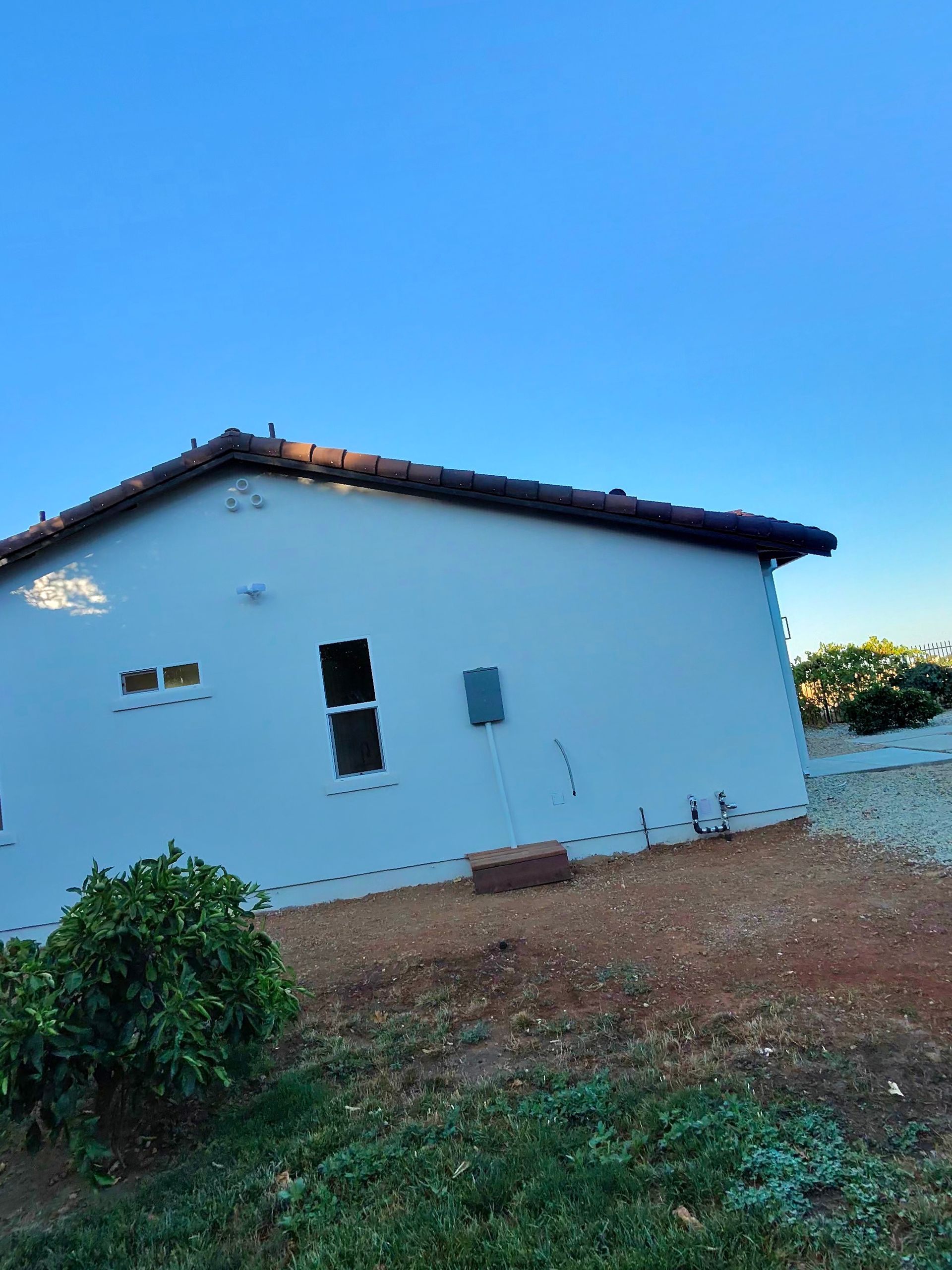 Small white house with a dark roof on a bare dirt lot under a clear blue sky