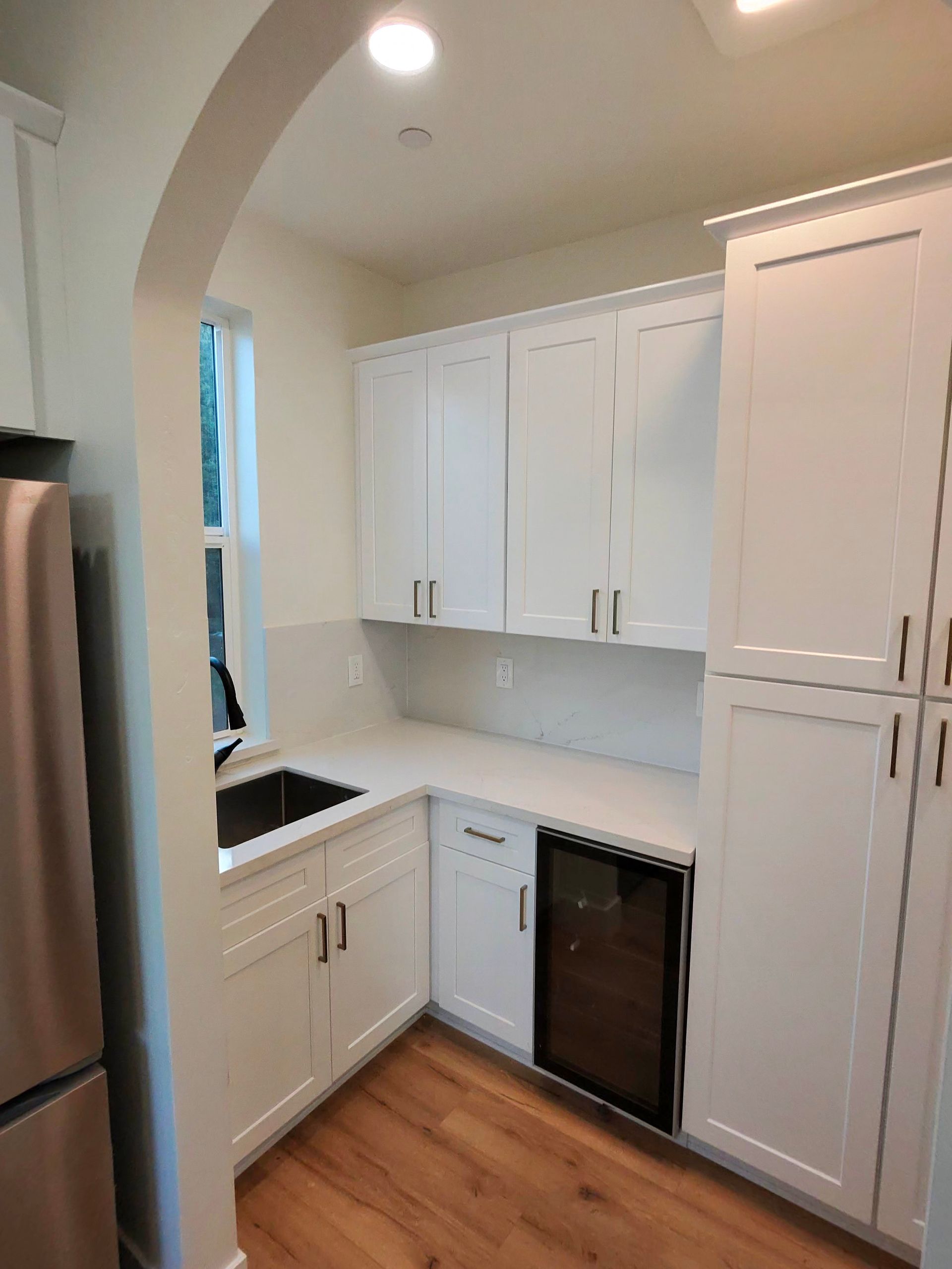 Compact white kitchen with cabinets, black dishwasher, wood floor, and arched doorway