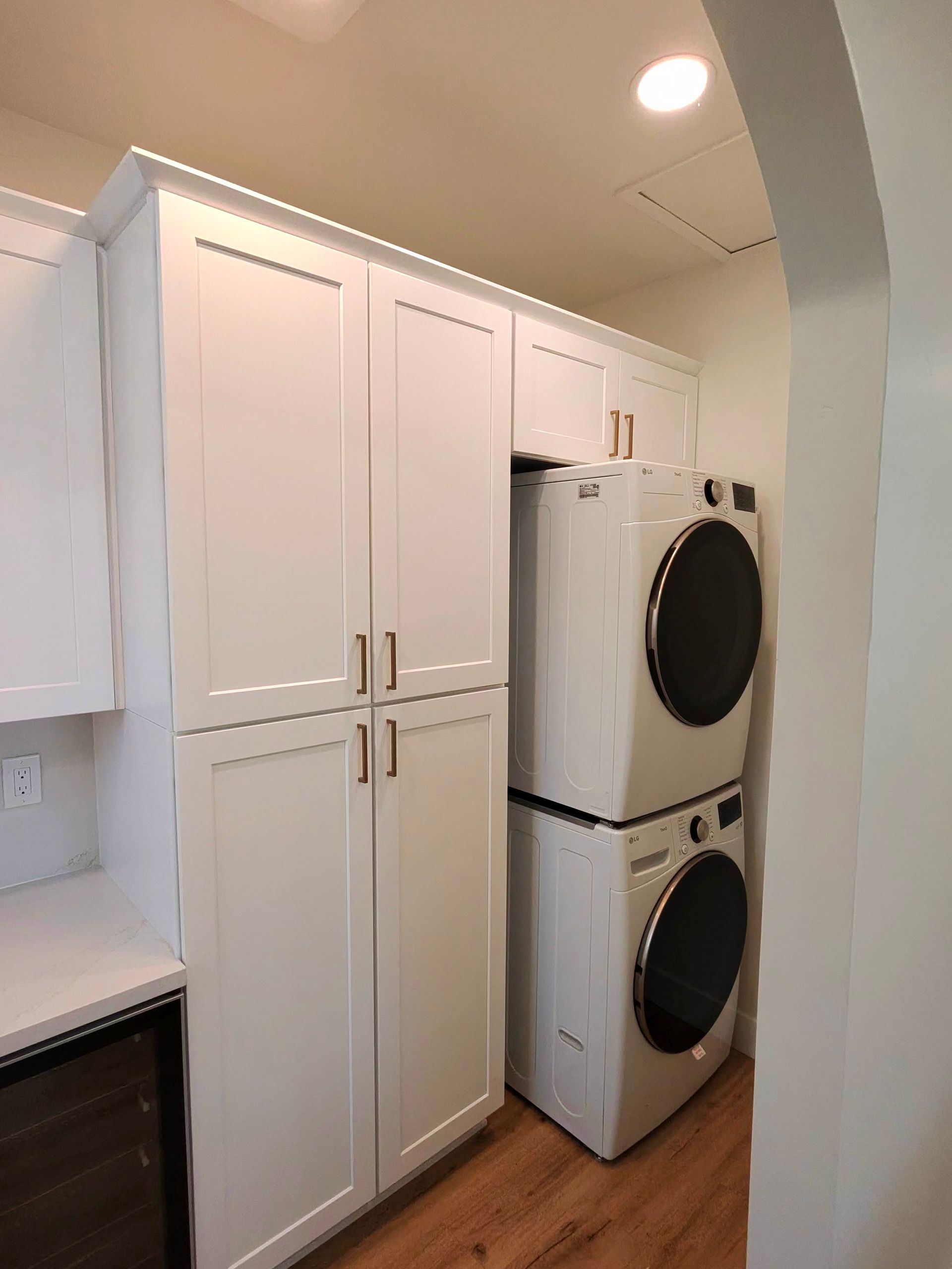 Laundry room with stacked washer and dryer beside white cabinets and a countertop.