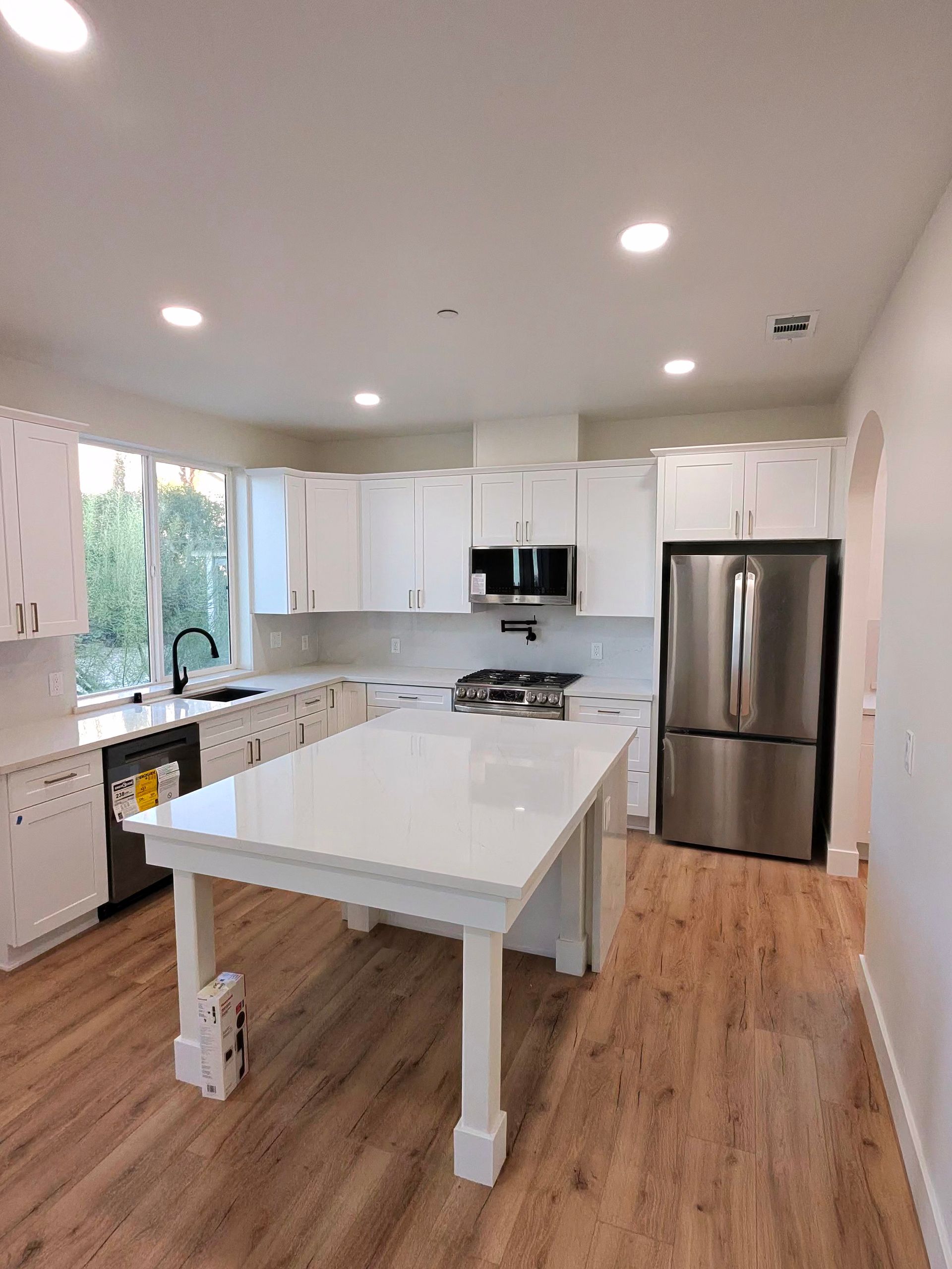 Bright modern kitchen with white cabinets, central island, stainless-steel fridge, and wood floors