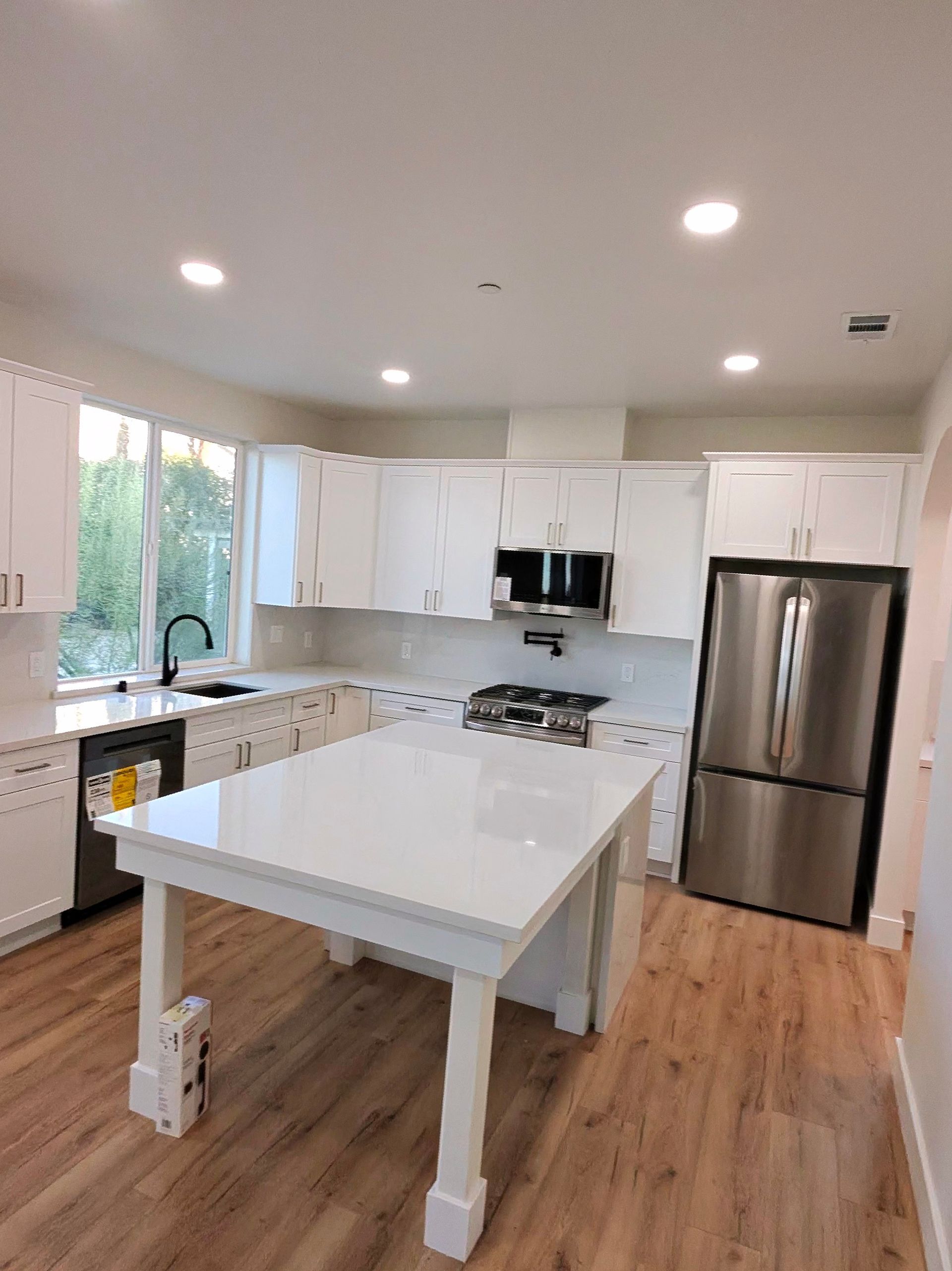 Bright white modern kitchen with island, stainless steel fridge, and wood floors