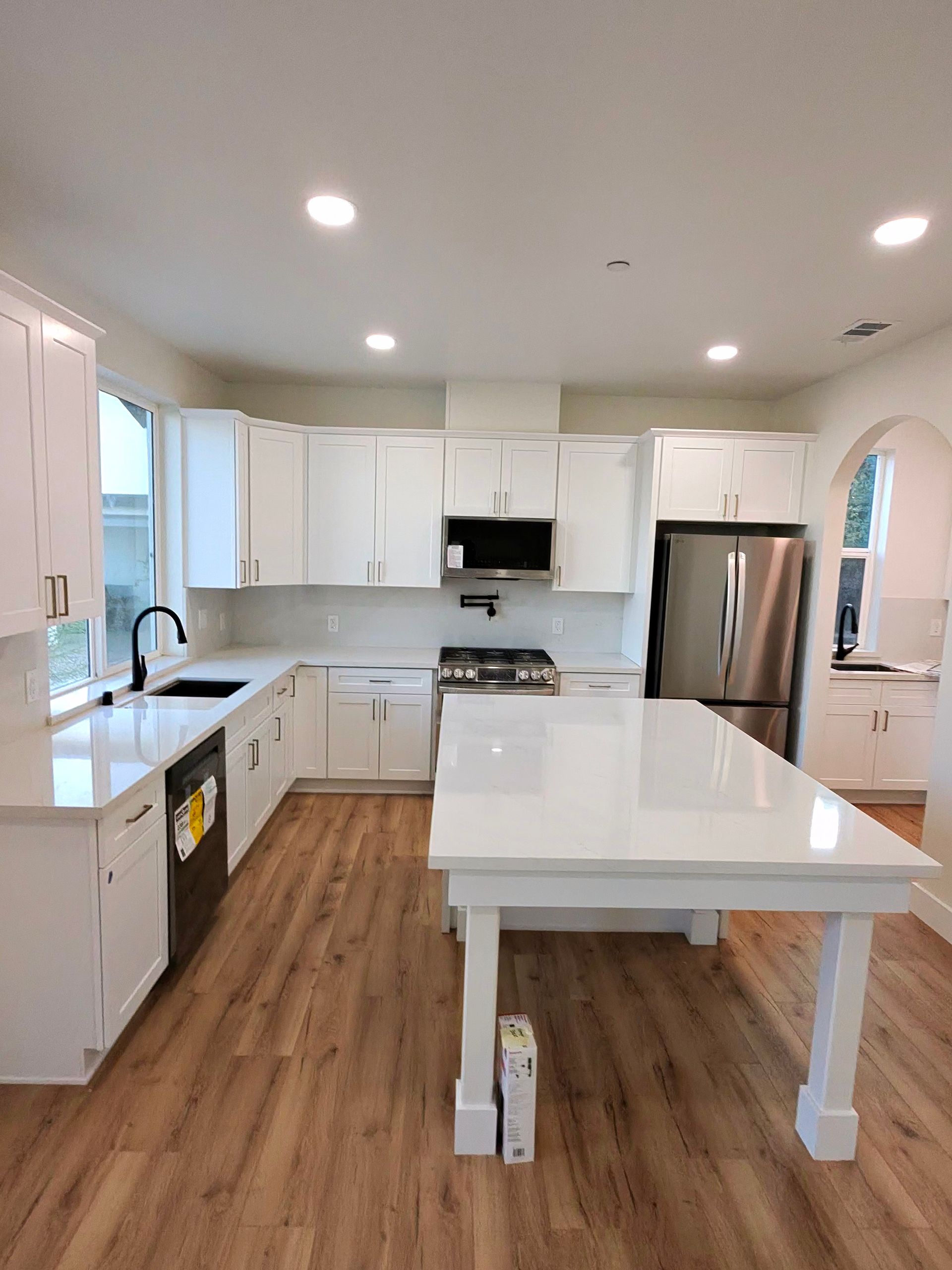 Bright modern kitchen with white cabinets, island, stainless appliances, and wood flooring.