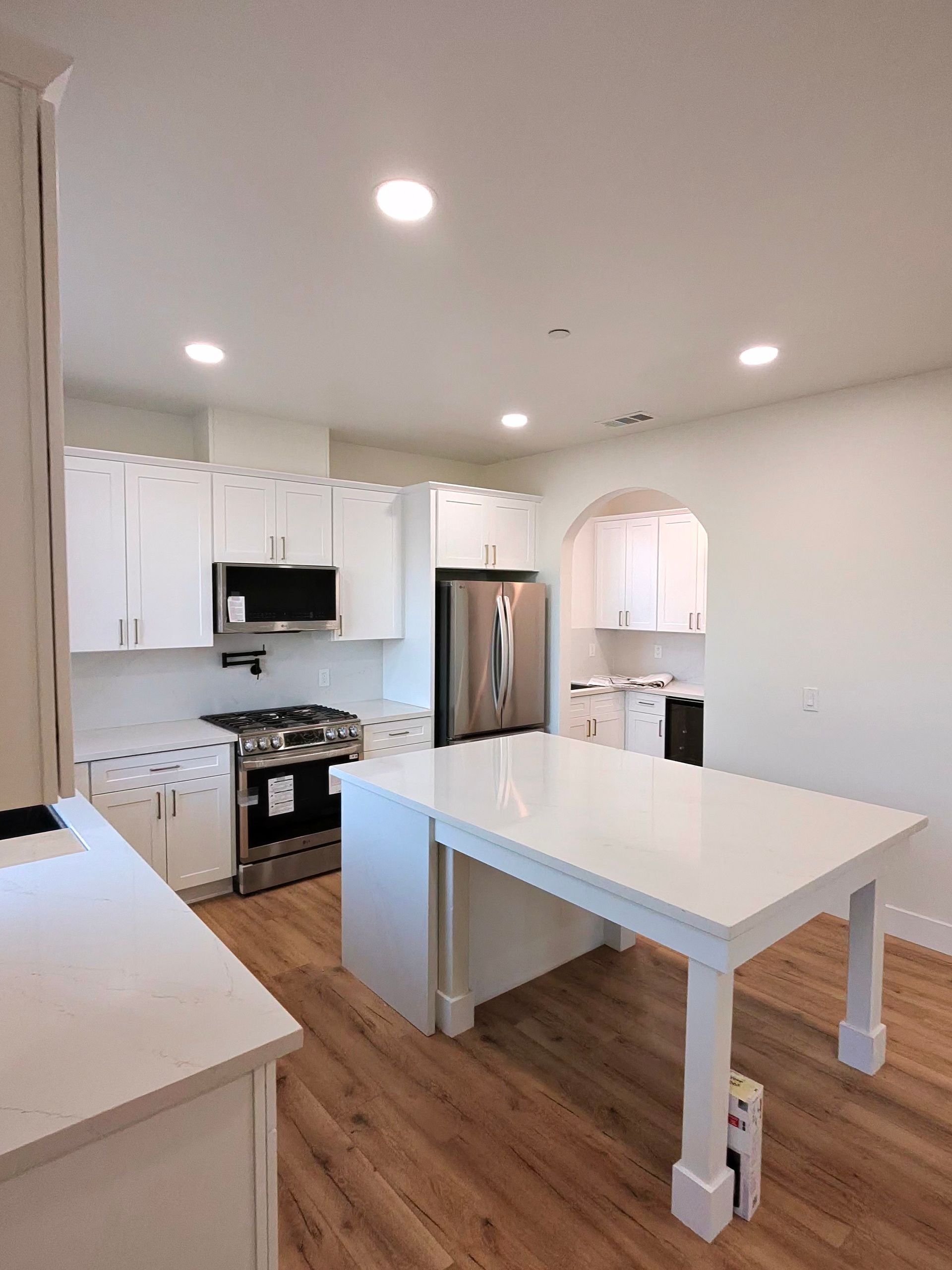 Bright modern kitchen with white cabinets, stainless fridge, and a white island on wood floors
