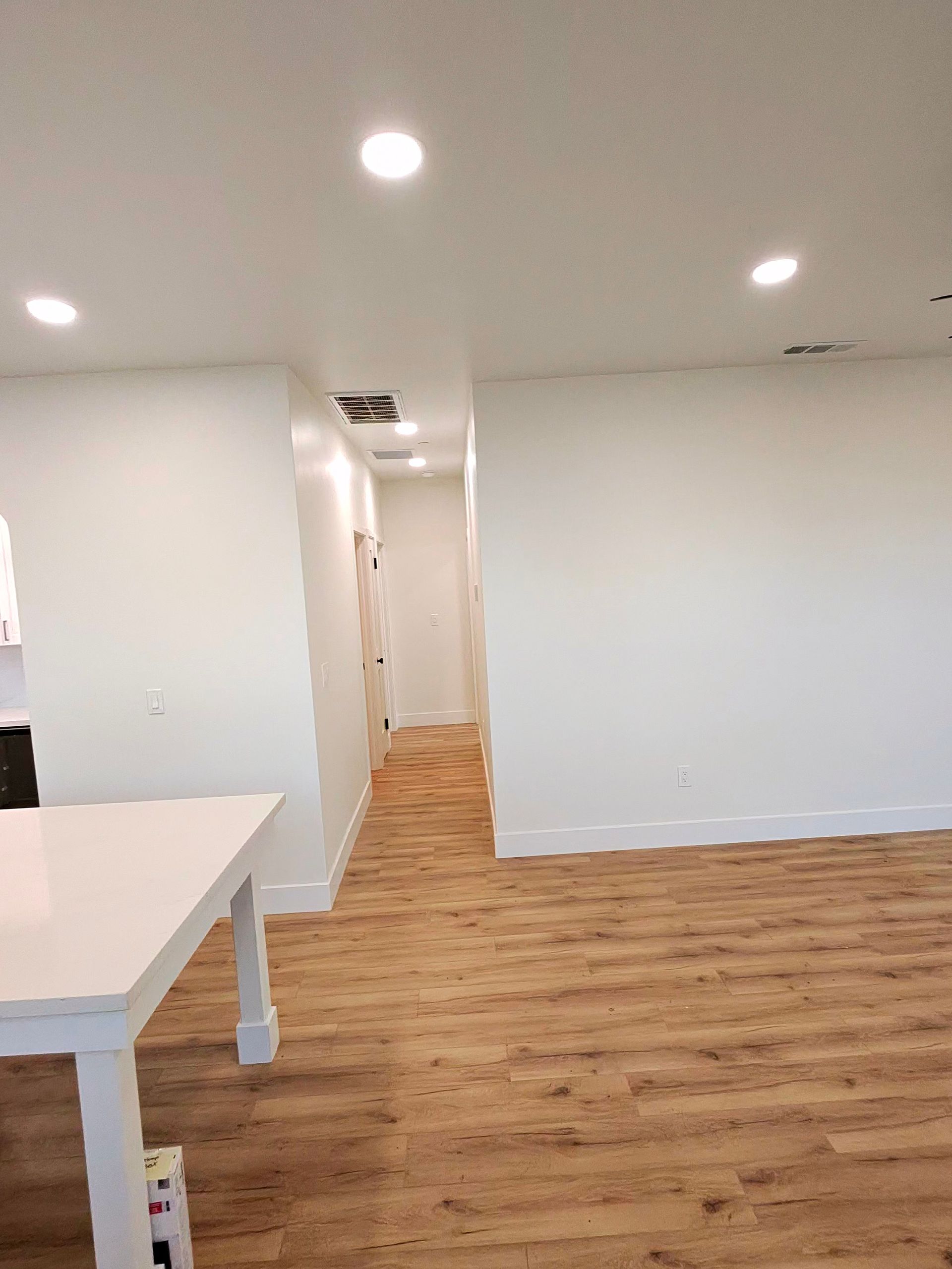 Bright empty office hallway with white walls, recessed lights, and wood flooring
