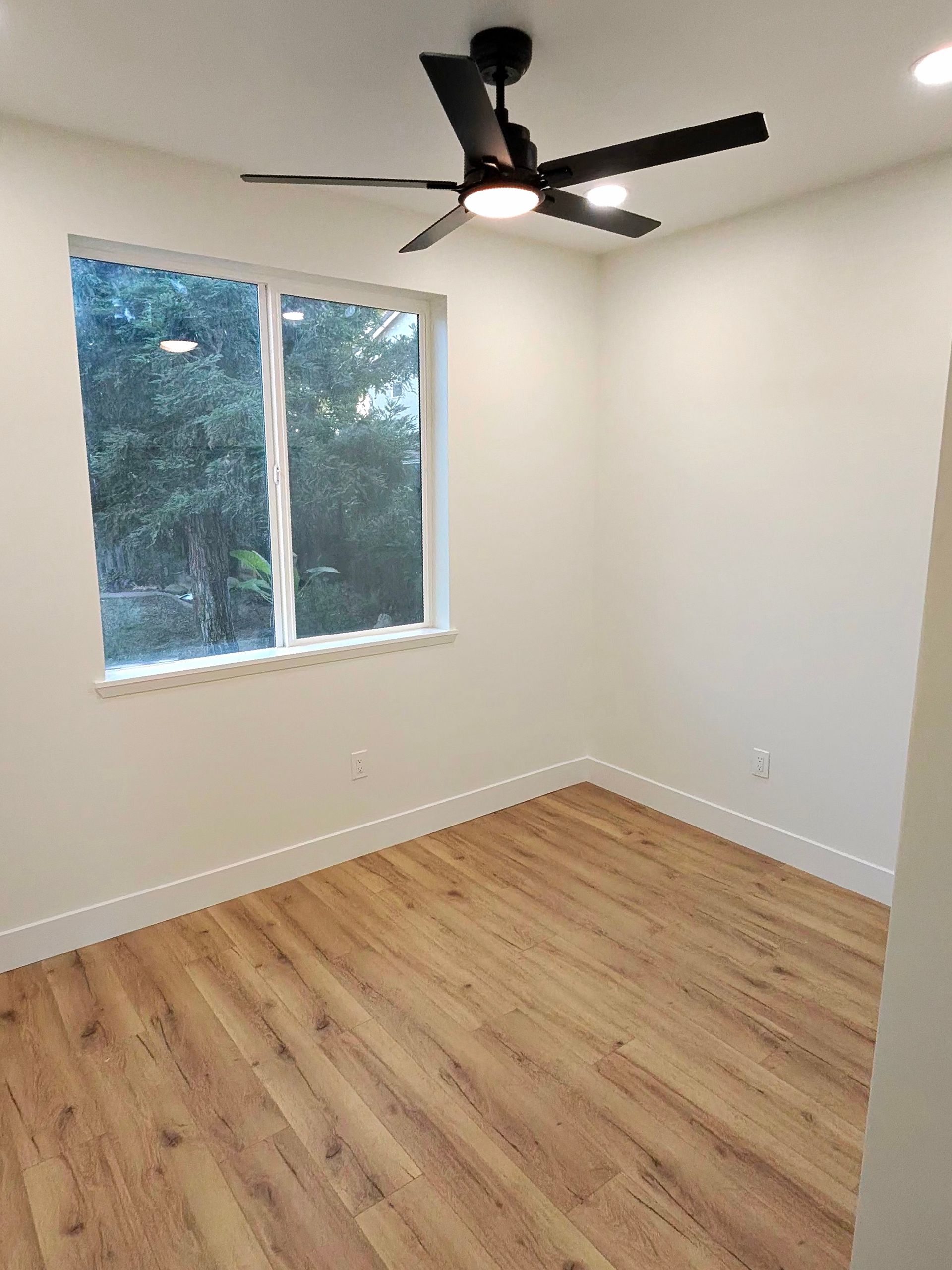 Empty bedroom with wood floors, white walls, a window, and a ceiling fan
