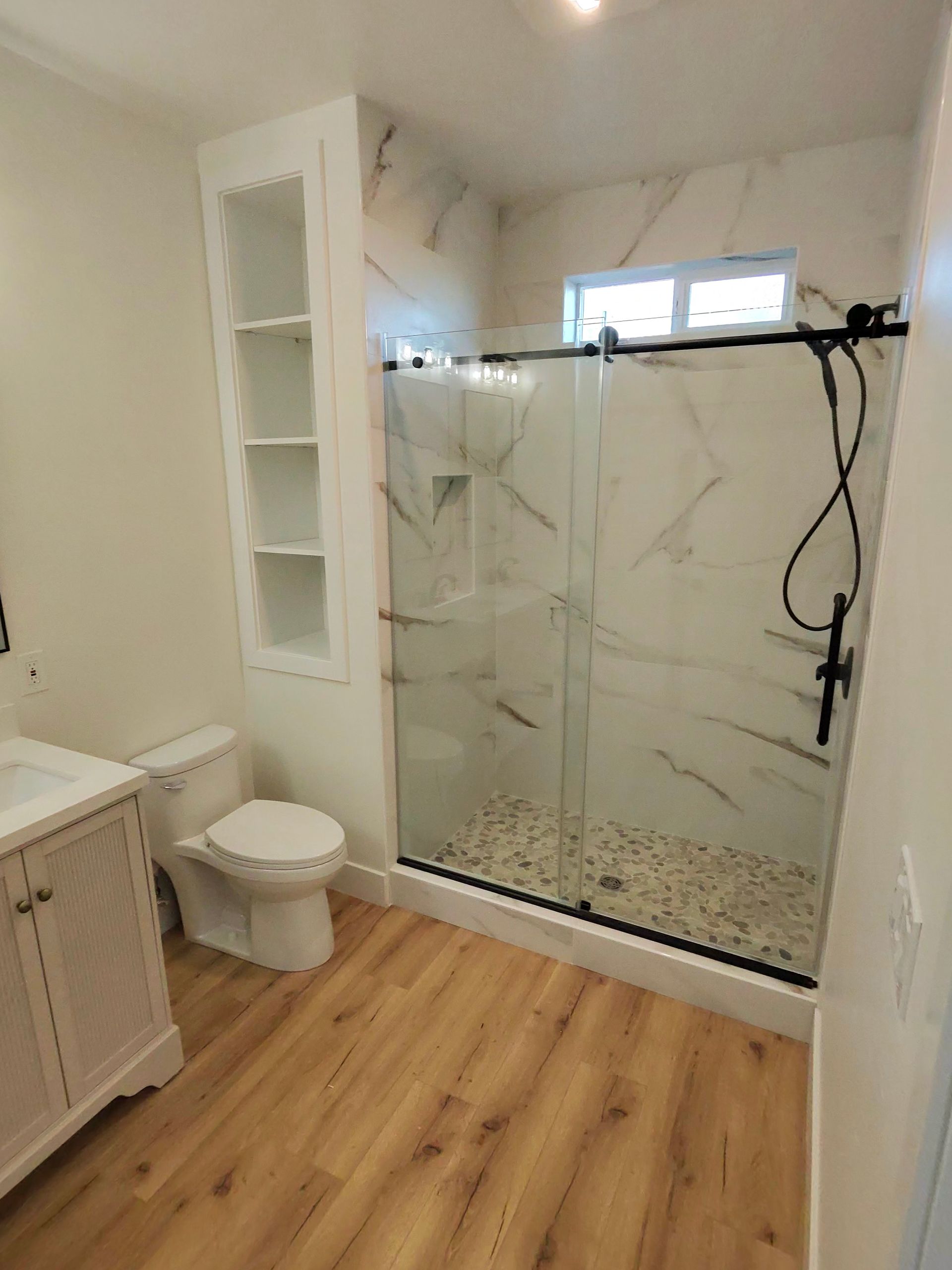 Small bathroom with glass shower, white toilet, vanity, and wood-look floor.