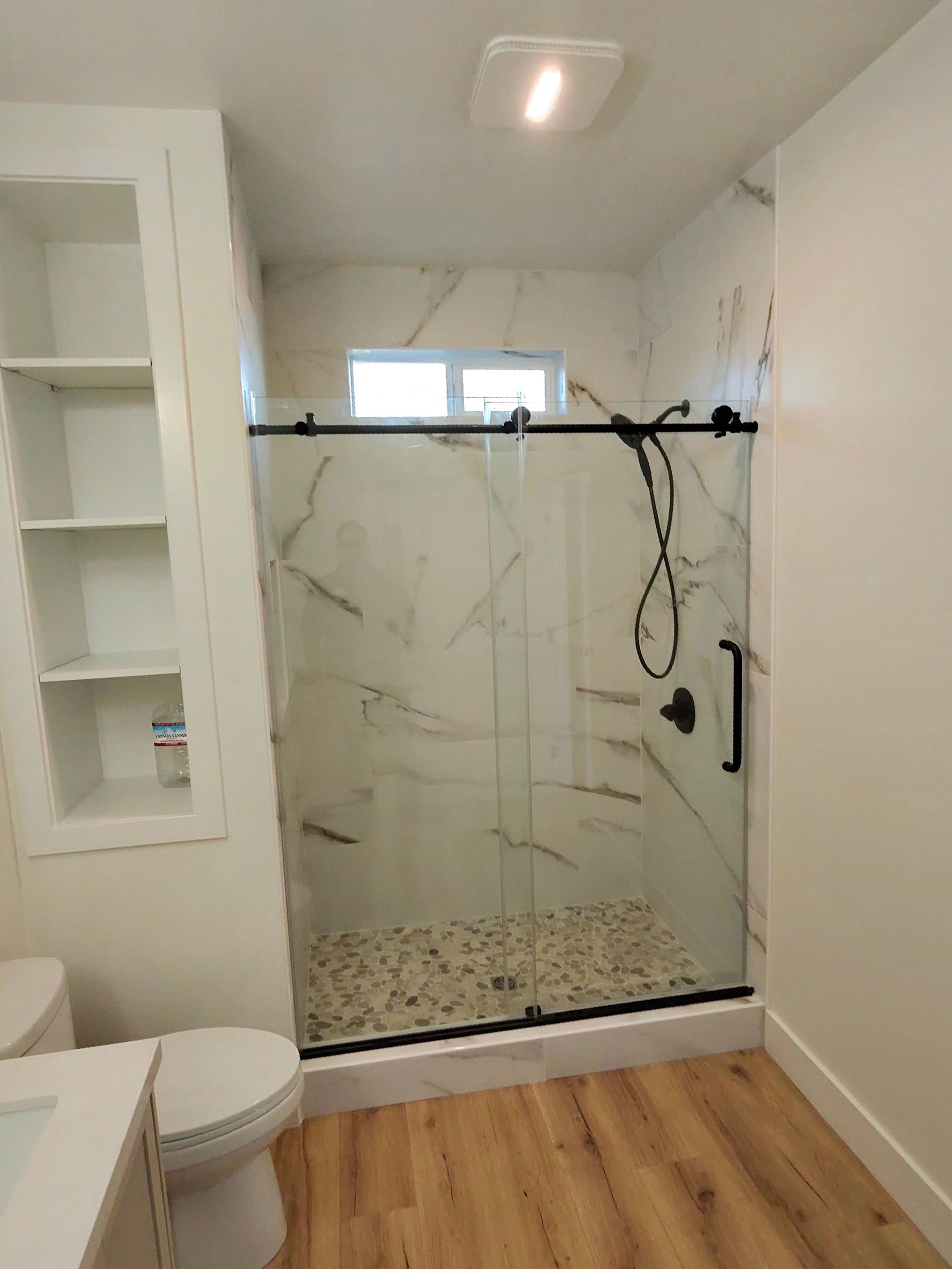 Modern bathroom with walk-in shower, white marble-look tile, glass door, and wood floor.