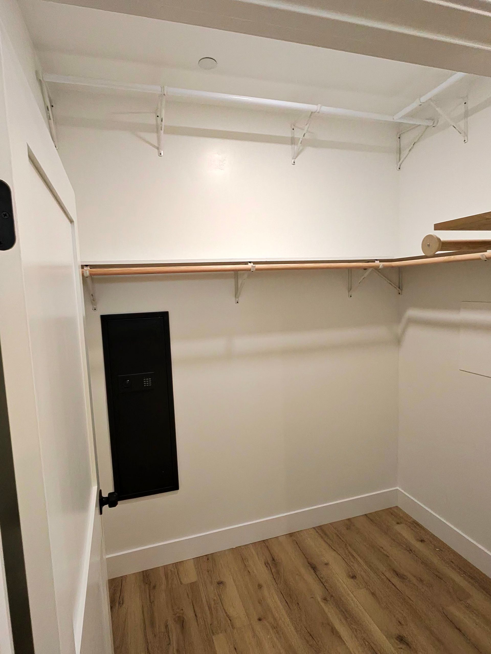 Empty walk-in closet with white walls, wood floor, and hanging rods.