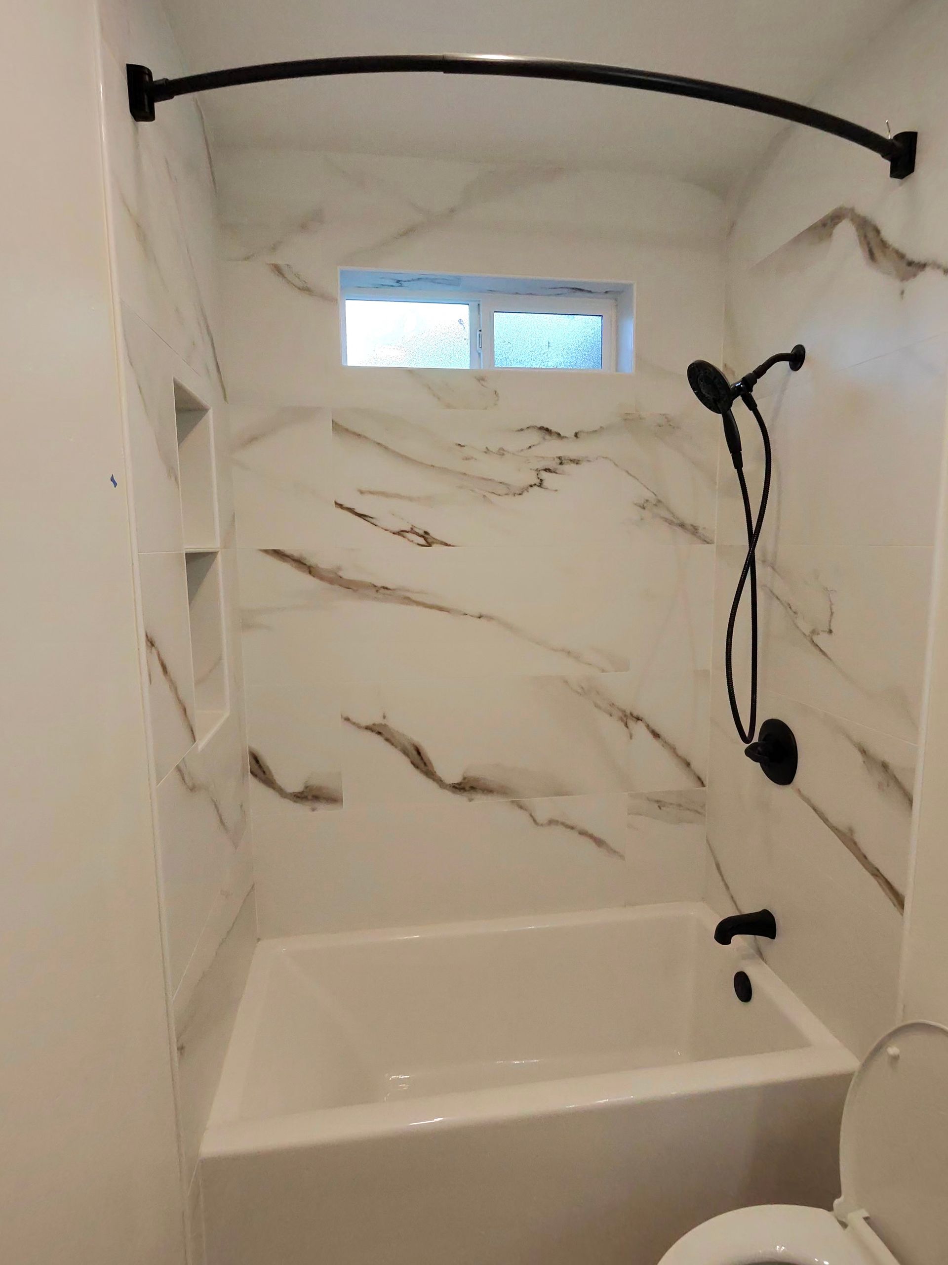 Small modern bathroom with marble-look shower/tub, window, grab bar, and handheld showerhead