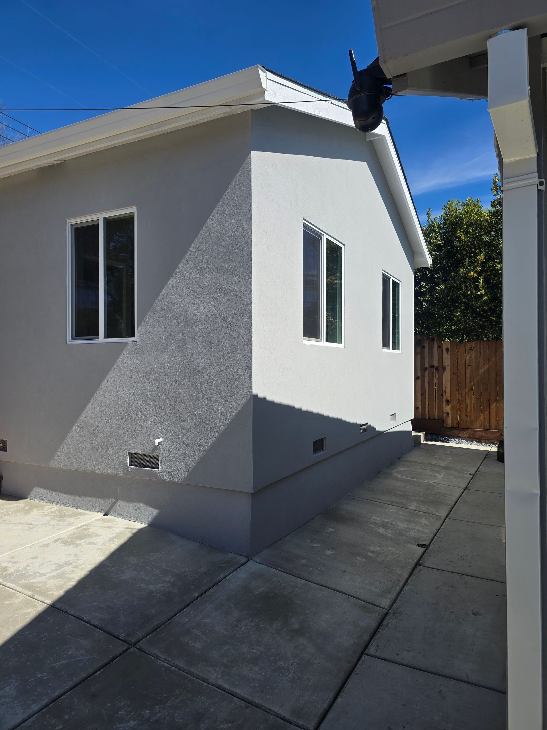 White stucco house exterior with two windows and a paved driveway under a clear blue sky