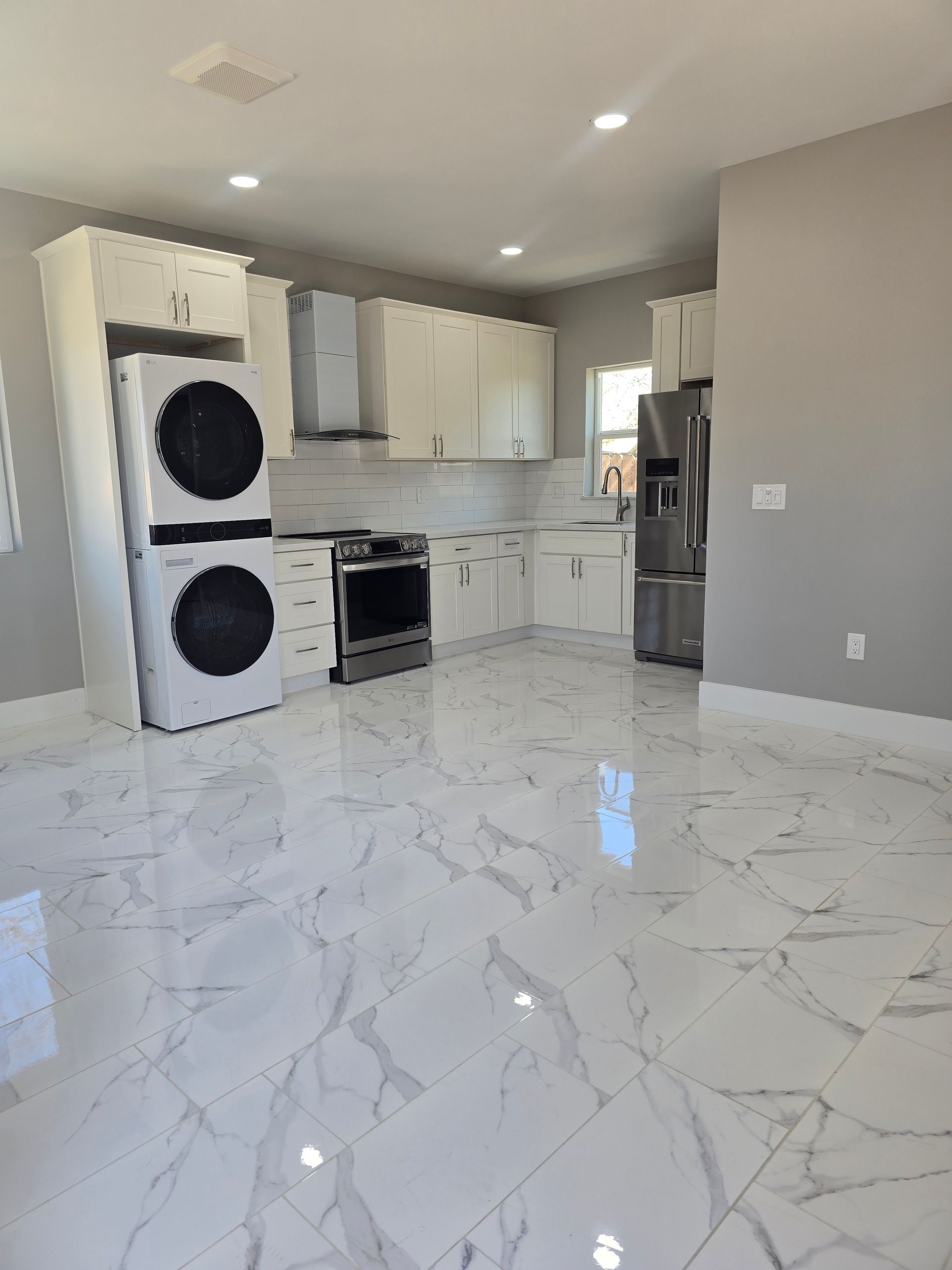Bright modern kitchen with white cabinets, black appliances, and glossy marble-pattern tile floor.