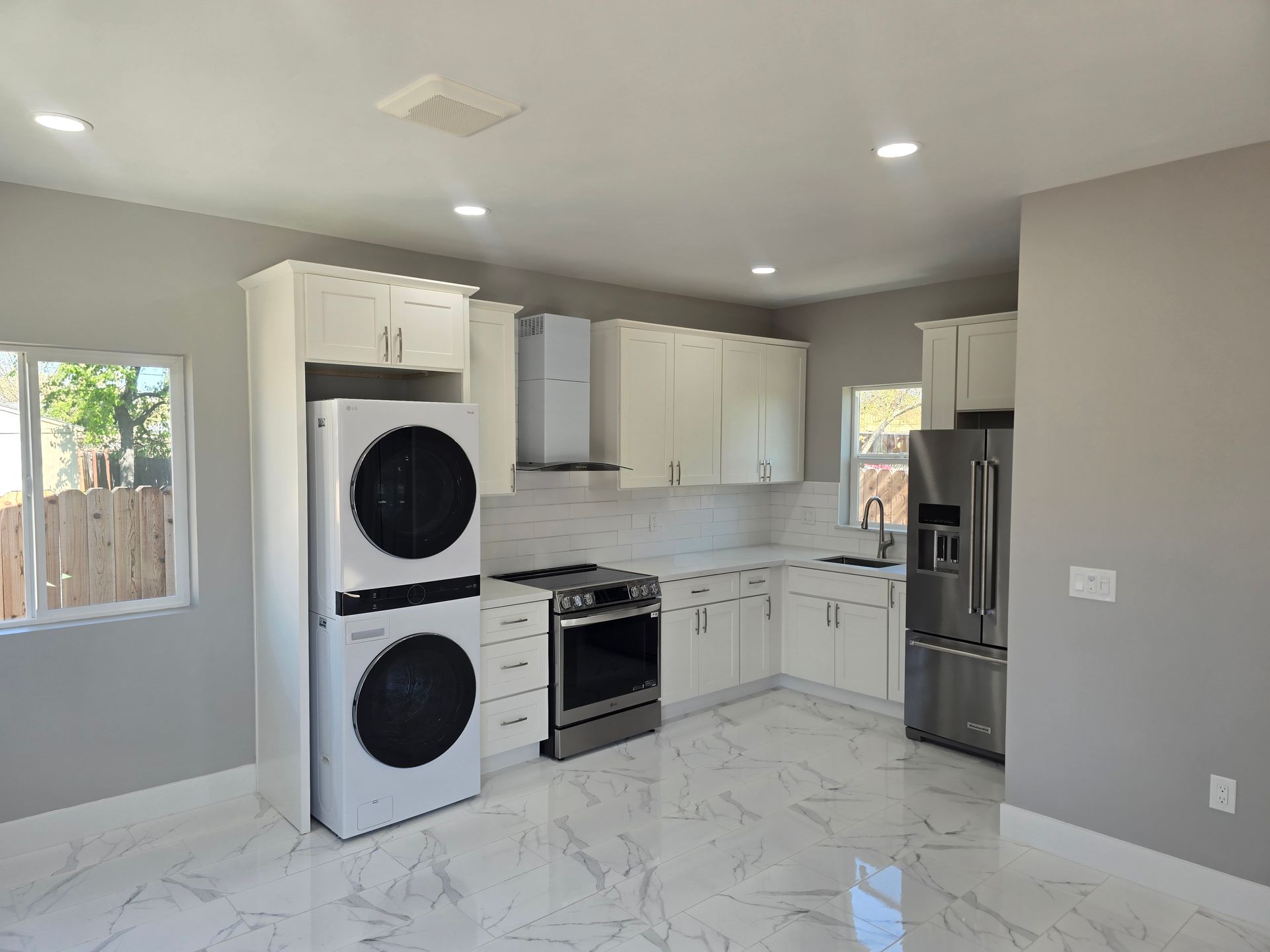 Bright kitchen with white cabinets, stainless appliances, marble-look floor, and stacked washer-dryer.