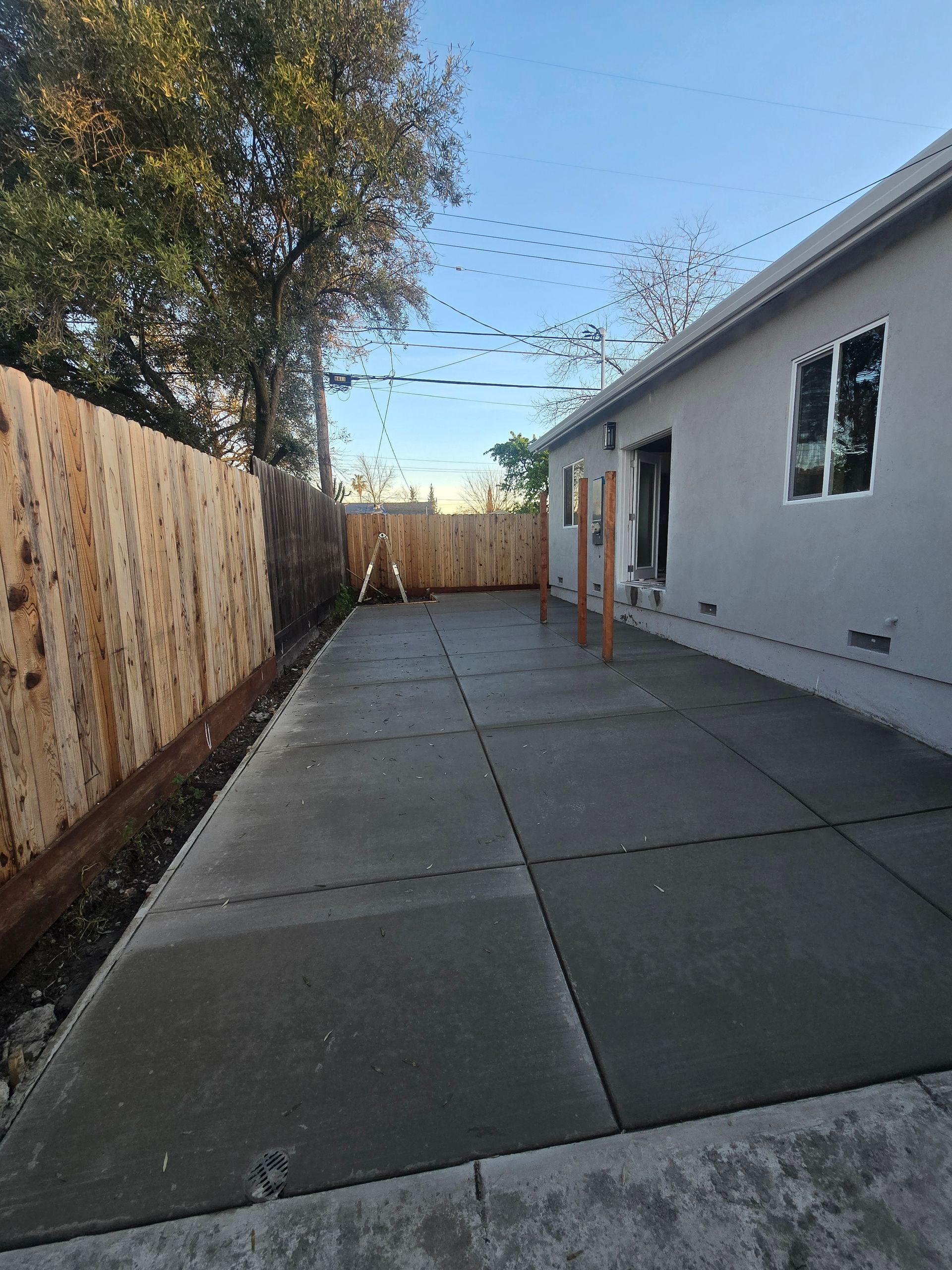 Backyard patio with concrete slabs, wooden fence, white house wall, and string lights overhead