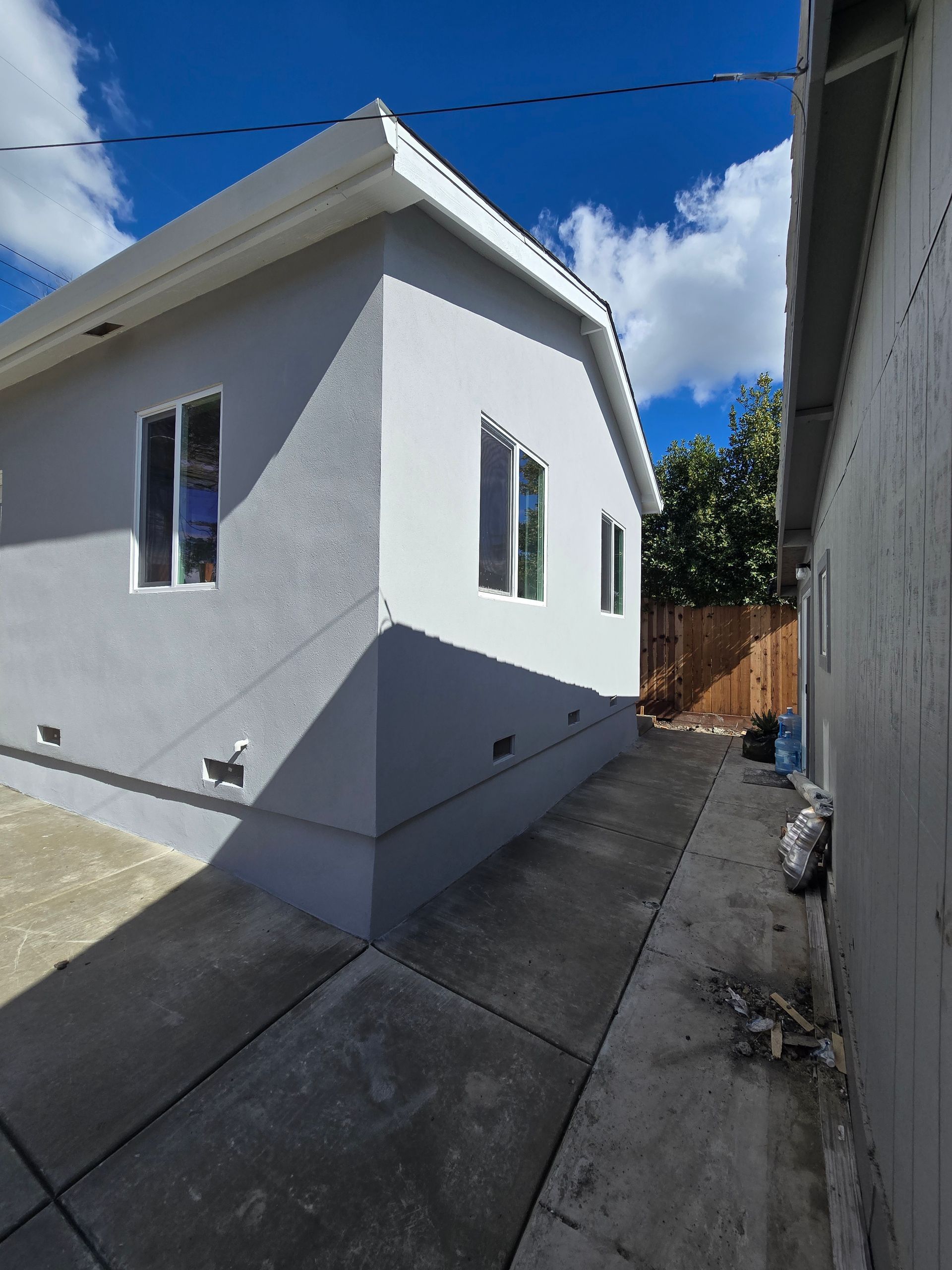 White house exterior with narrow side yard, concrete walkway, and blue sky with clouds