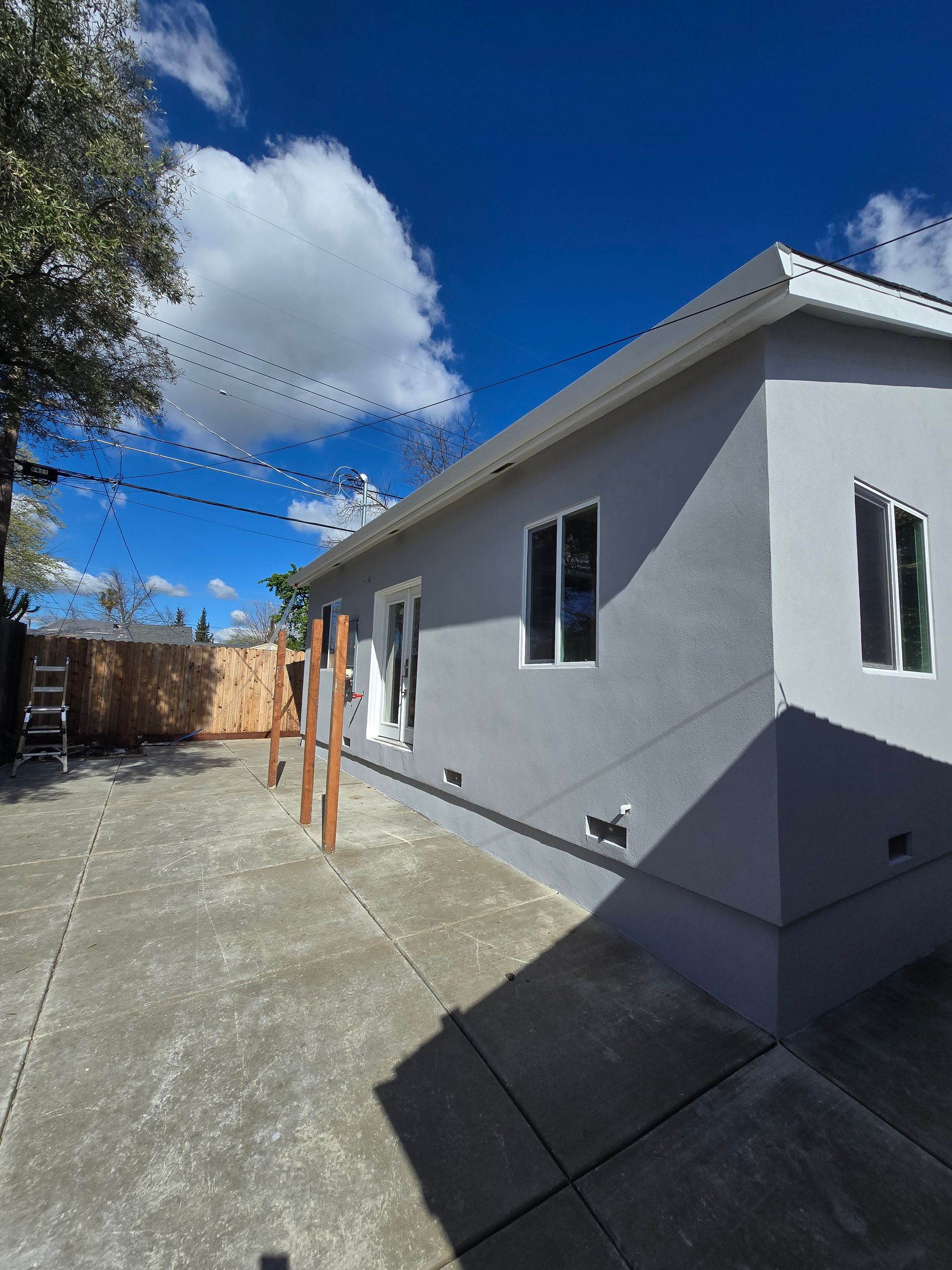 Gray house exterior with concrete driveway, orange posts, string lights, and blue sky with clouds