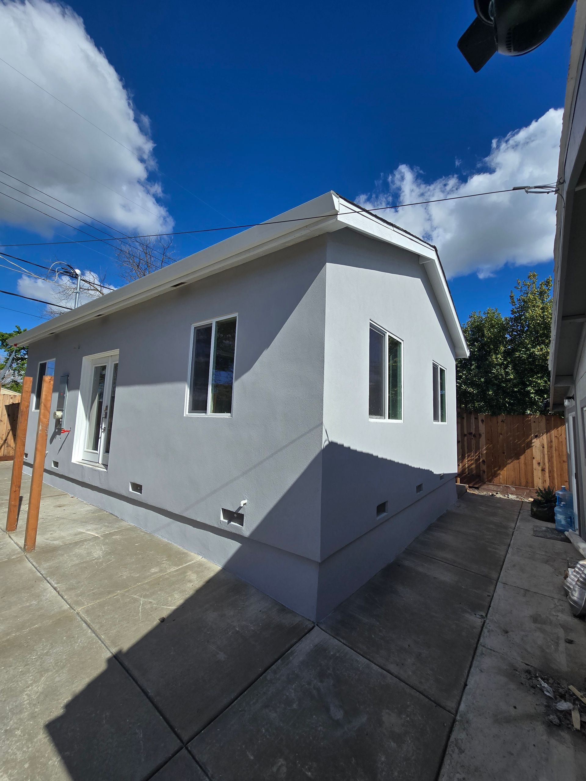 White single-story house exterior with gray trim, concrete driveway, and blue sky with clouds