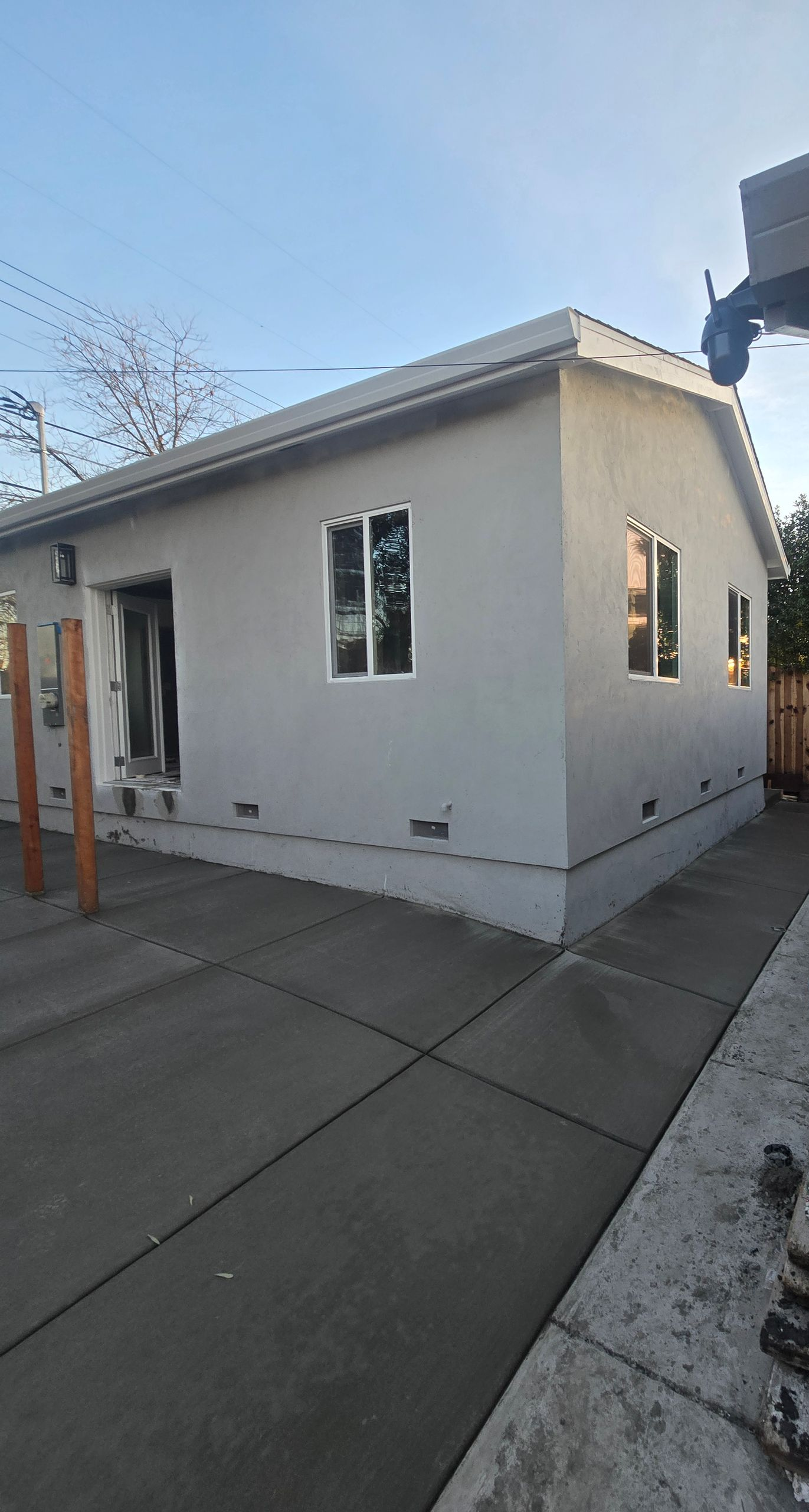 Backyard with a small white building, concrete driveway, and house wall on the right