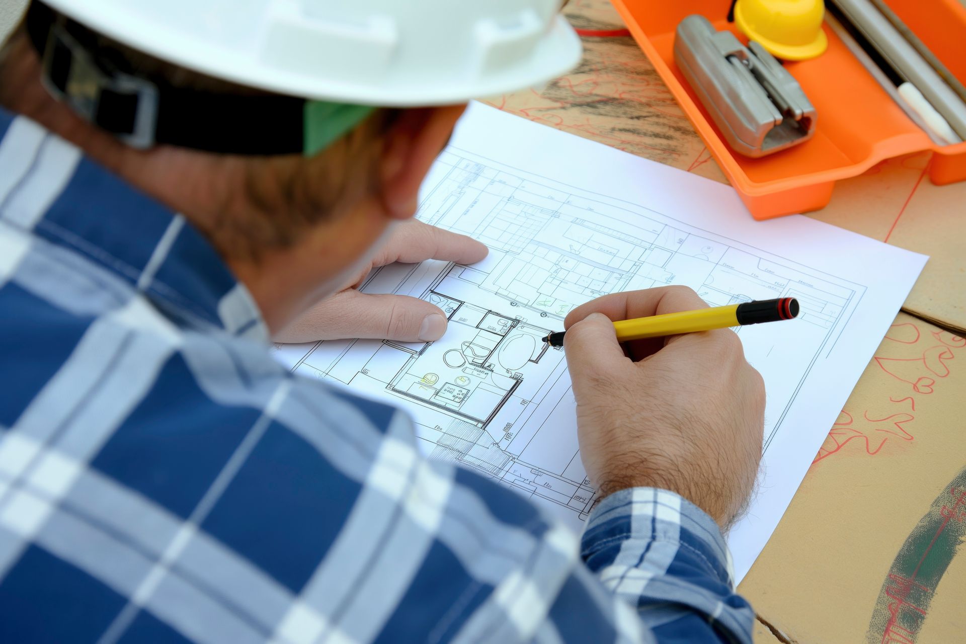 Construction worker sketching plans on a blueprint with a pencil at a desk
