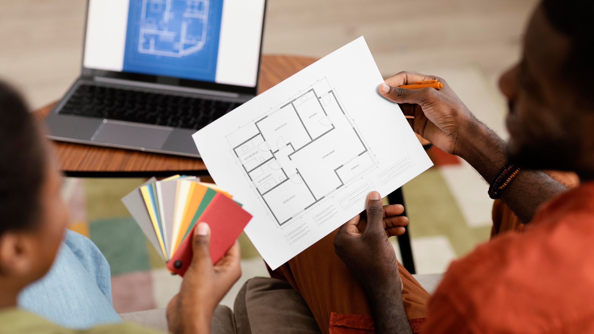 People reviewing a floor plan sketch and color swatches on a laptop in a design meeting