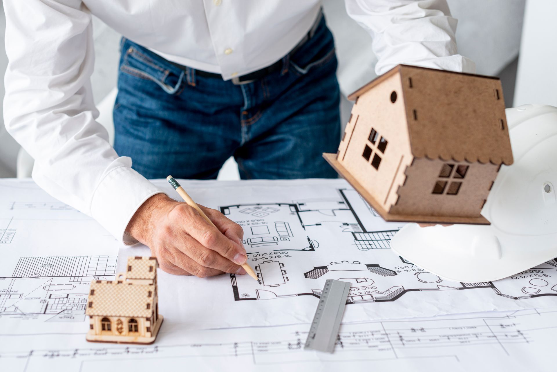 Person sketching house plans beside model homes on architectural blueprints