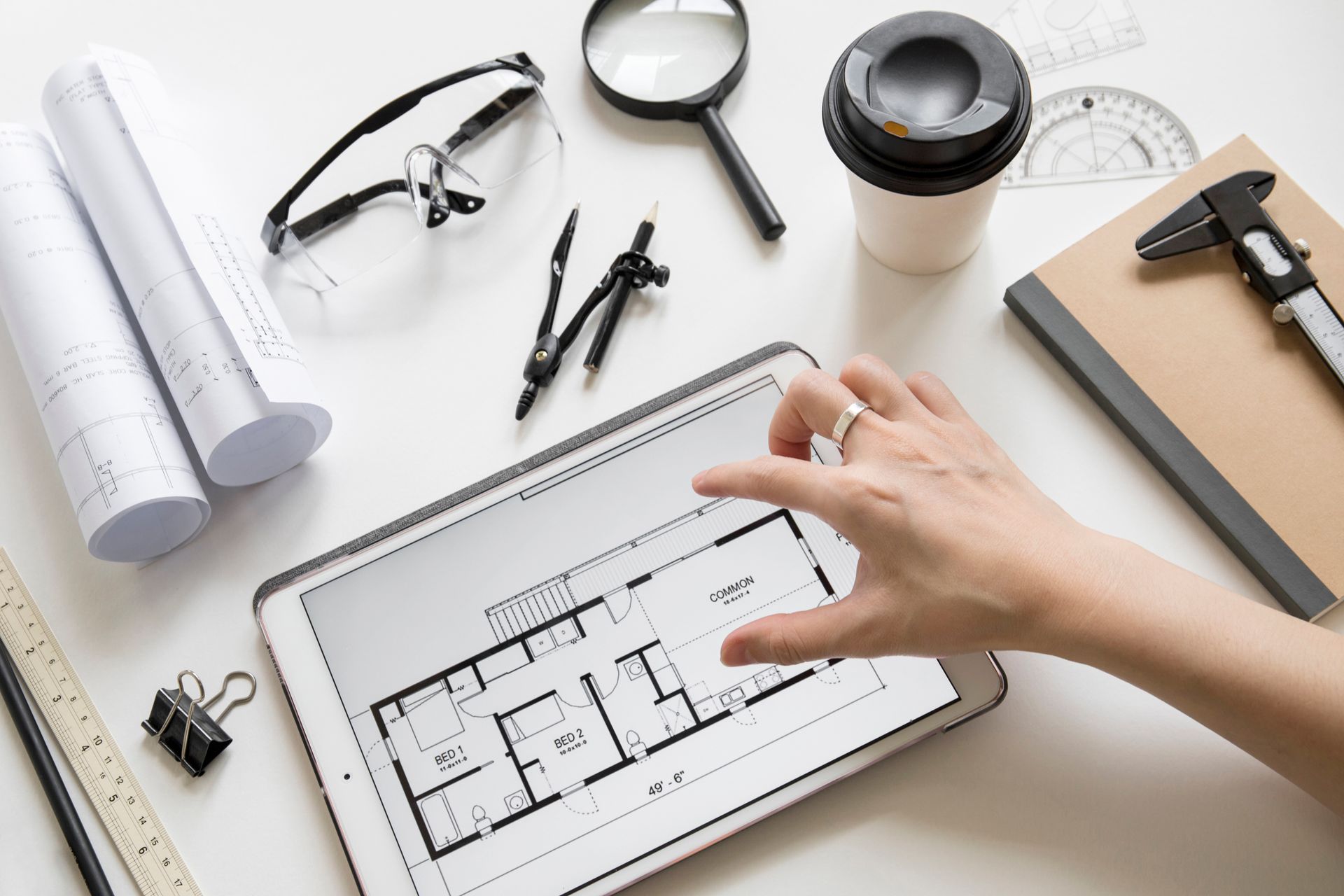 Architect reviewing floor plans on a tablet with drafting tools and coffee on a desk