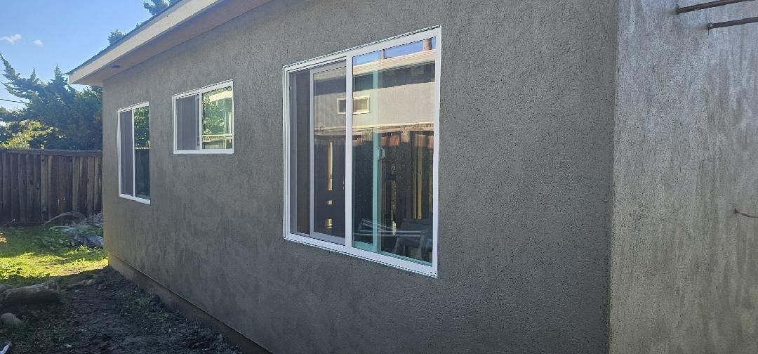 Exterior side view of a stucco house with two windows and a sliding glass door in daylight
