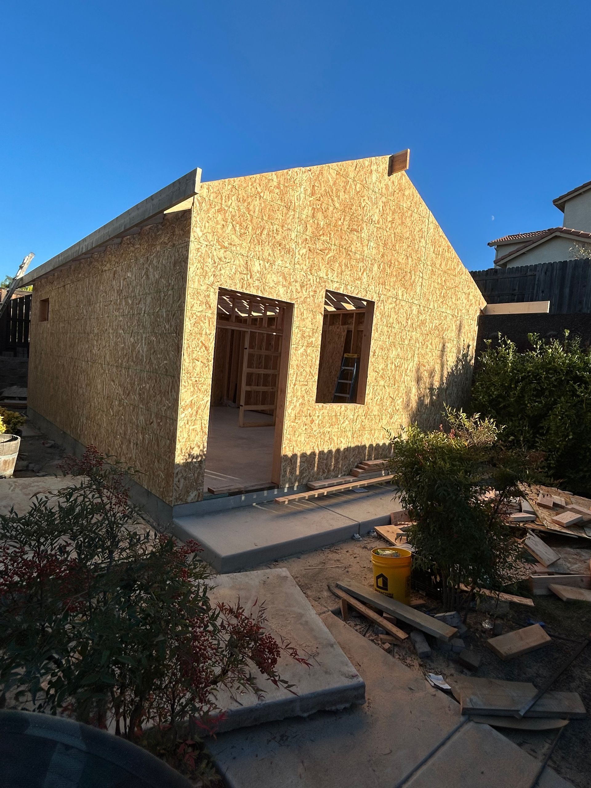 Small stone house under construction with a front porch and windows in a sunny yard
