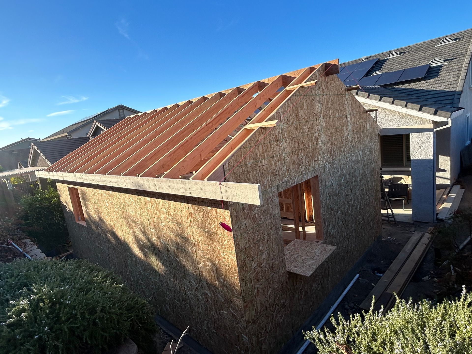 Small unfinished house with exposed OSB walls and a red roof under construction in a residential area