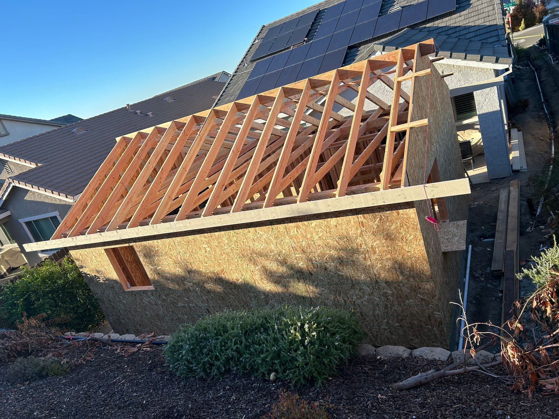 House under construction with exposed roof rafters and plywood sheathing in a suburban neighborhood