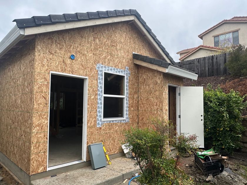 Small unfinished wooden shed with open door and window in a backyard, under construction