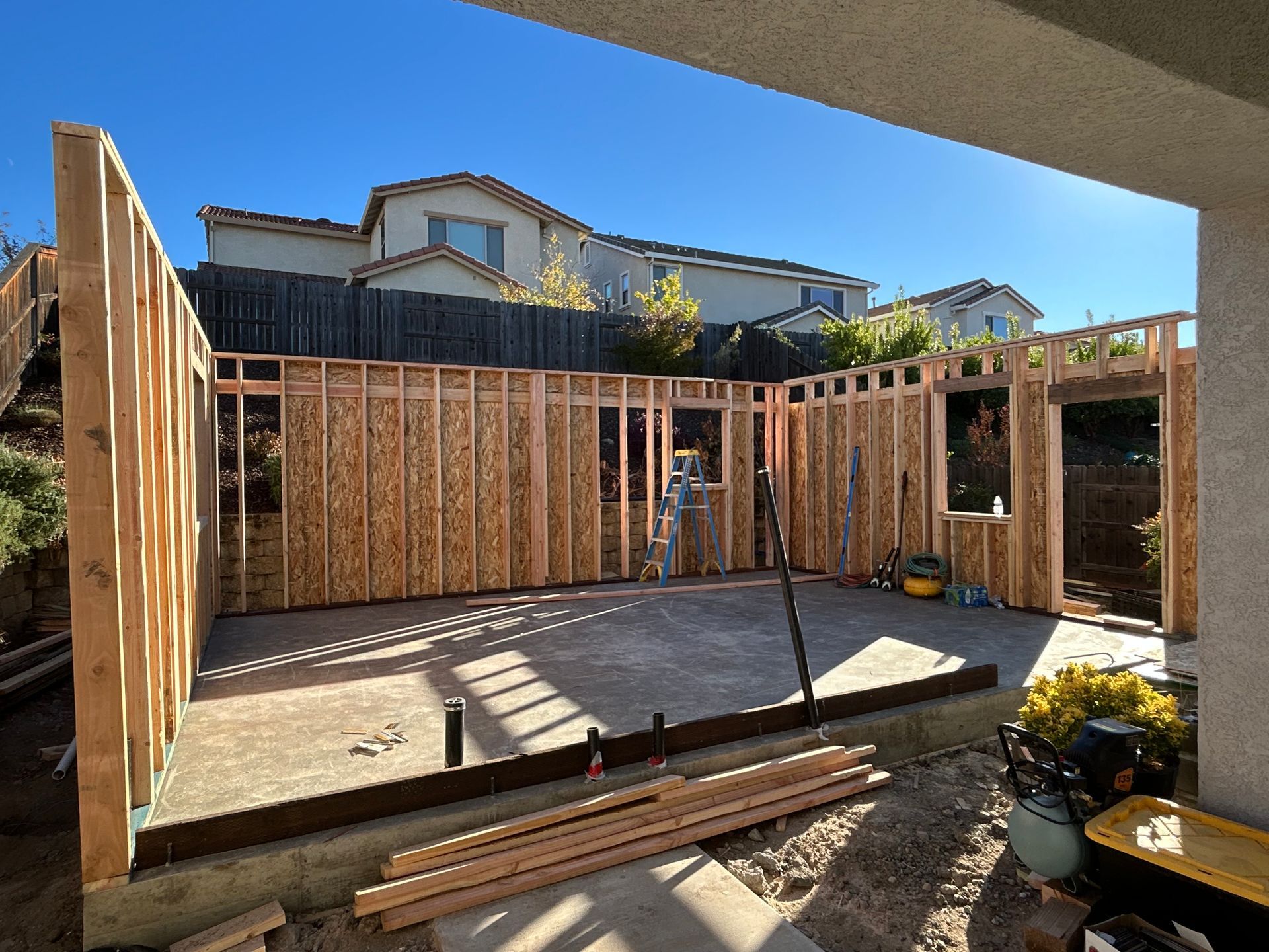 Unfinished wooden room addition with framed walls and concrete floor under construction in a backyard