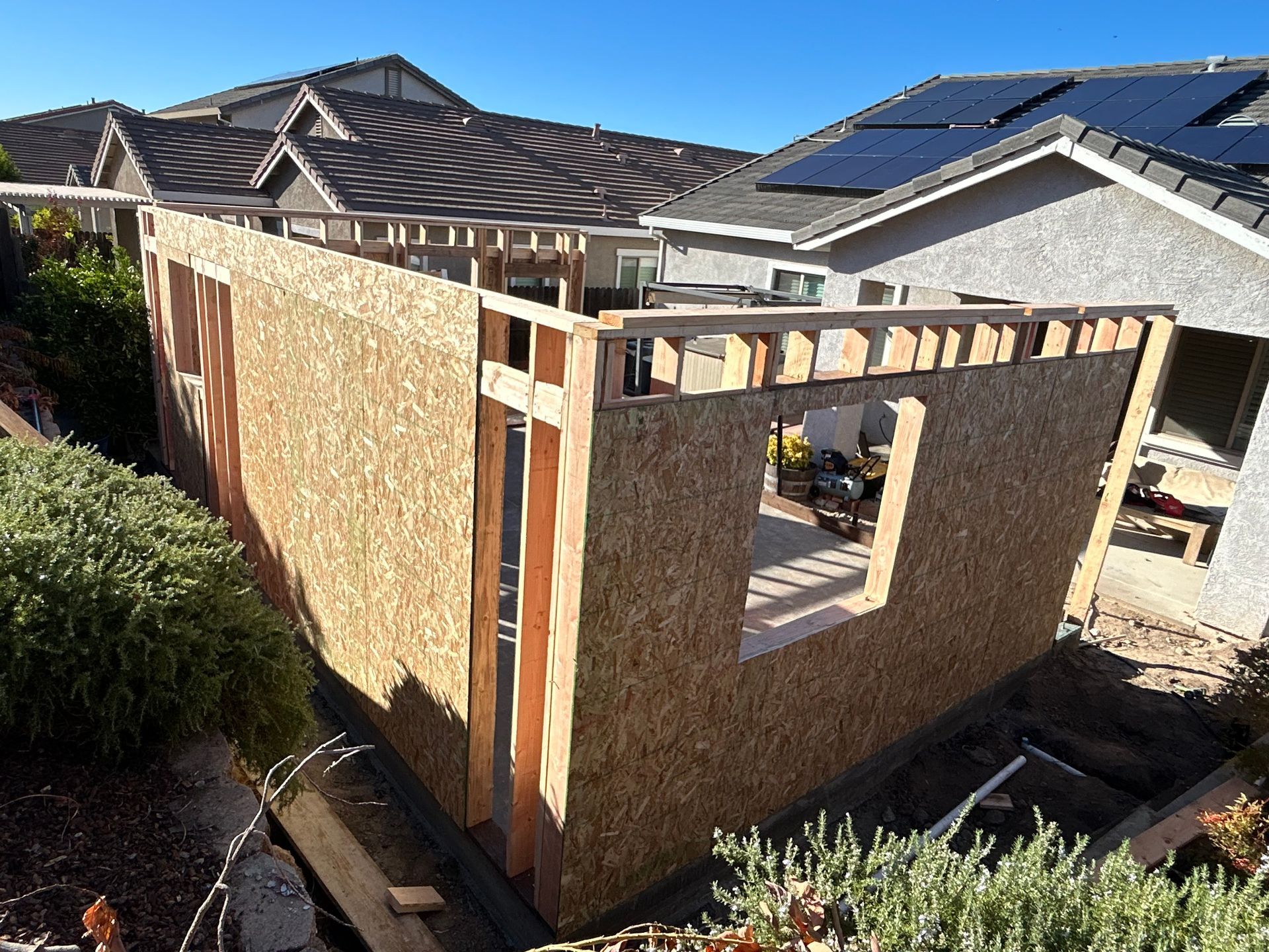 Partially built wooden house frame with OSB walls and a sloped roof under construction in a backyard