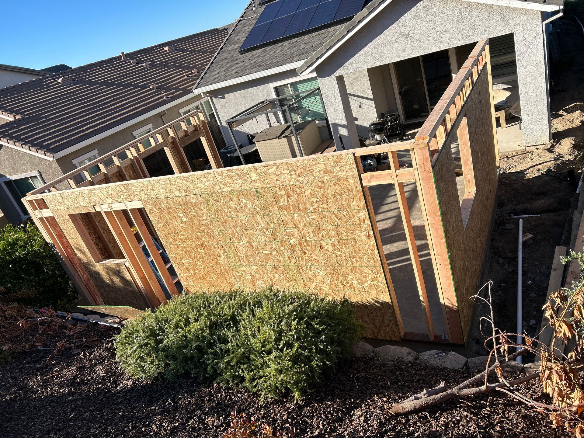 Partially built wooden fence around a house under construction, with a bush in front.