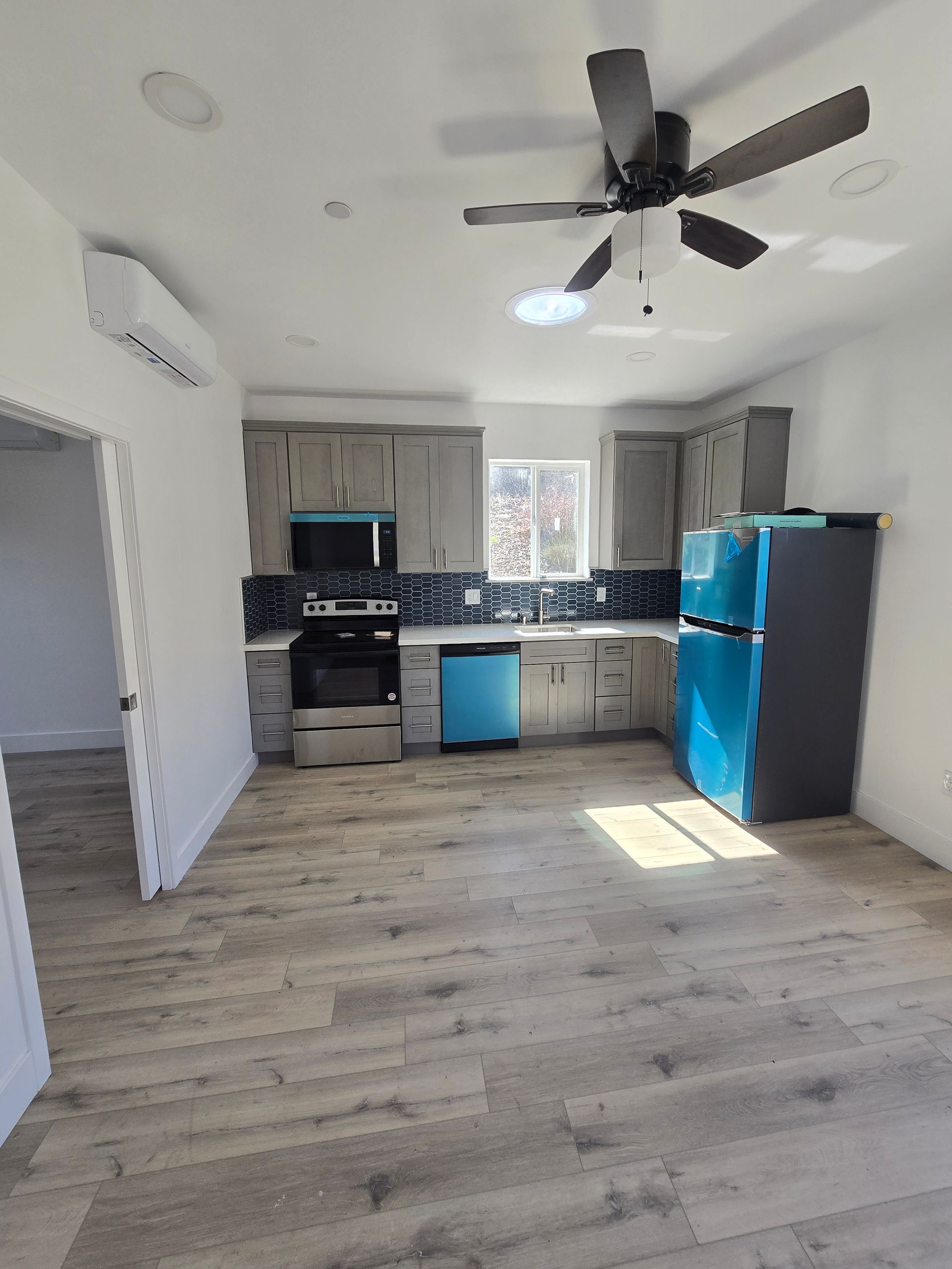 Empty kitchen with blue appliances, black counters, light wood floors, and a ceiling fan.