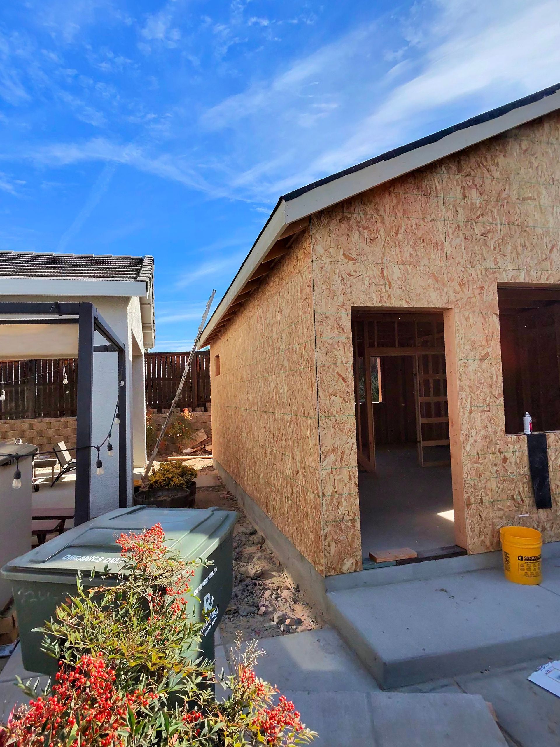 Outdoor construction site with a stucco house under renovation, open doorway, and blue sky