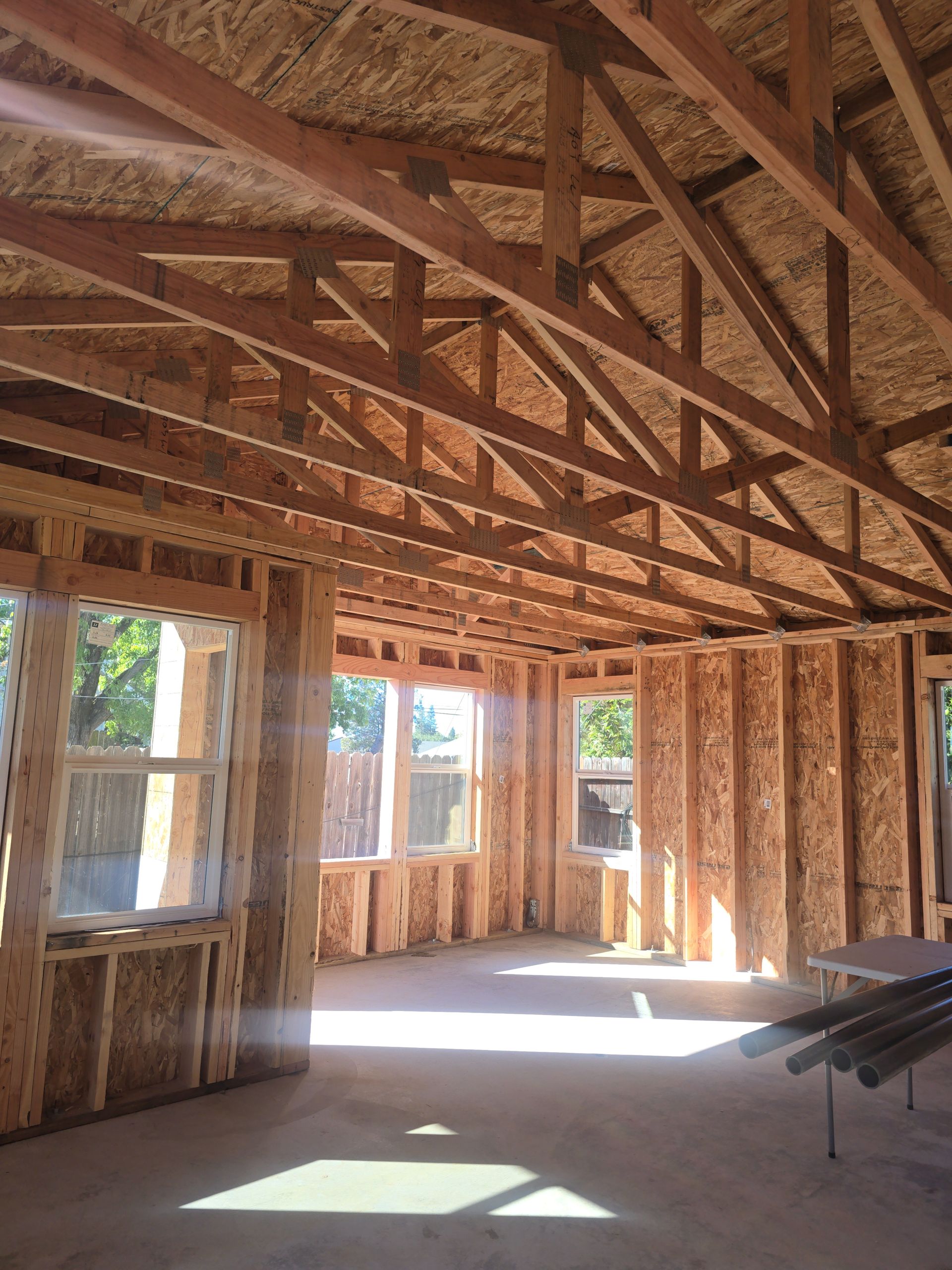Unfinished wooden house interior with exposed roof trusses, window openings, and sunlight on the floor