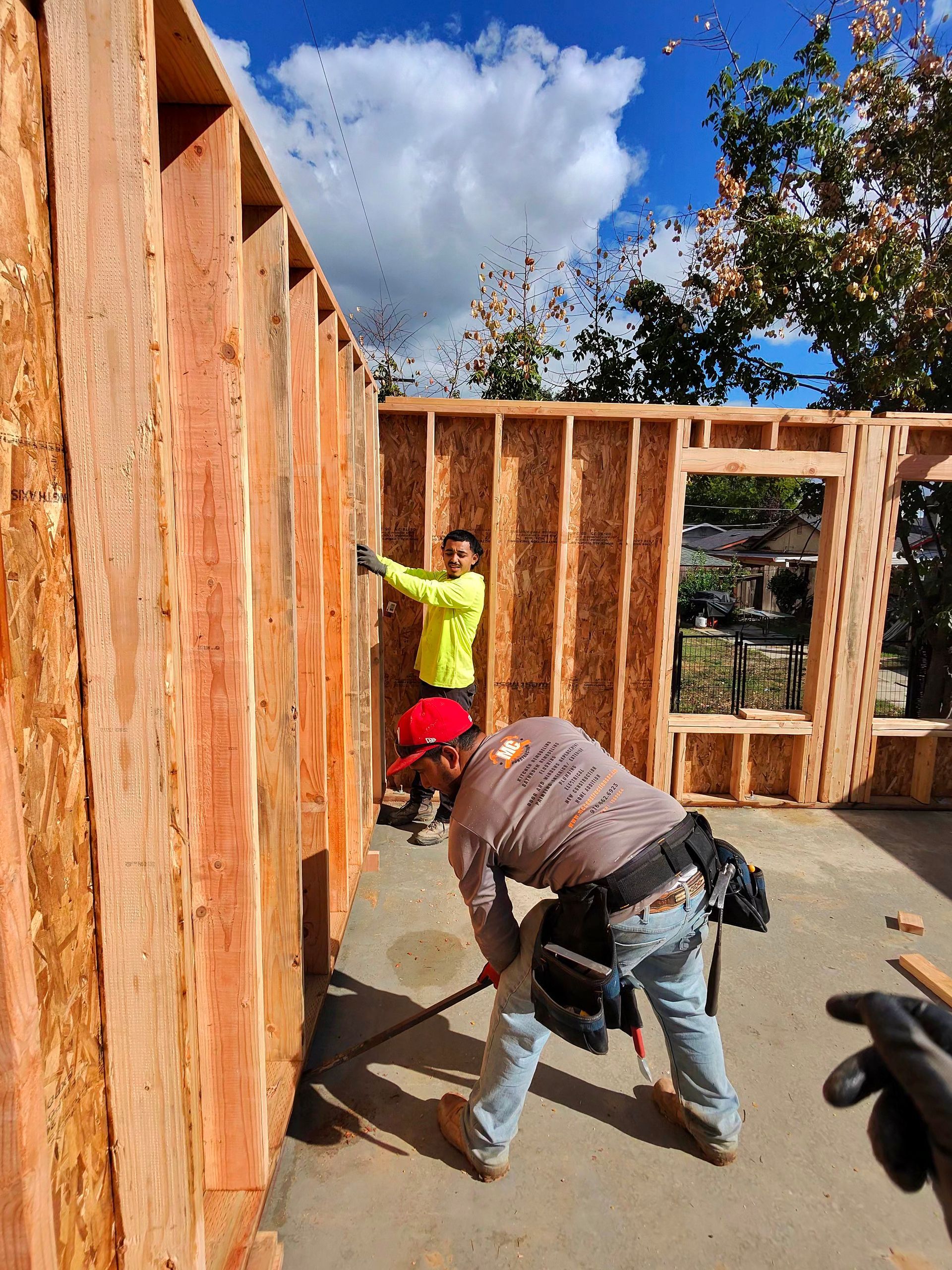 Workers framing a house interior with wooden studs on a sunny construction site.