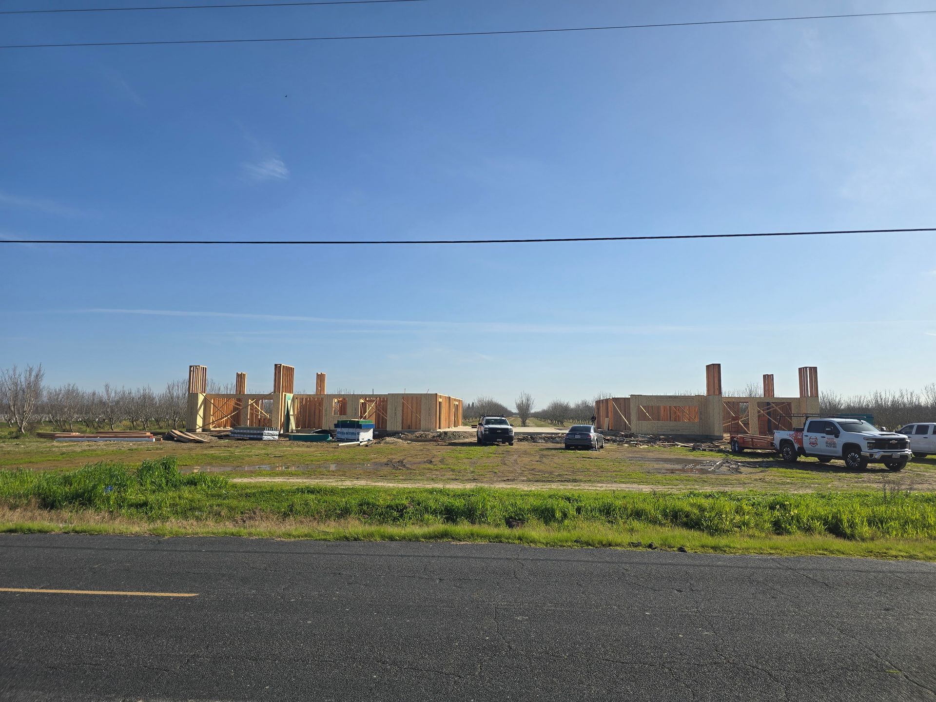 Scattered brick ruins in a grassy field under a clear blue sky, with cars parked nearby.