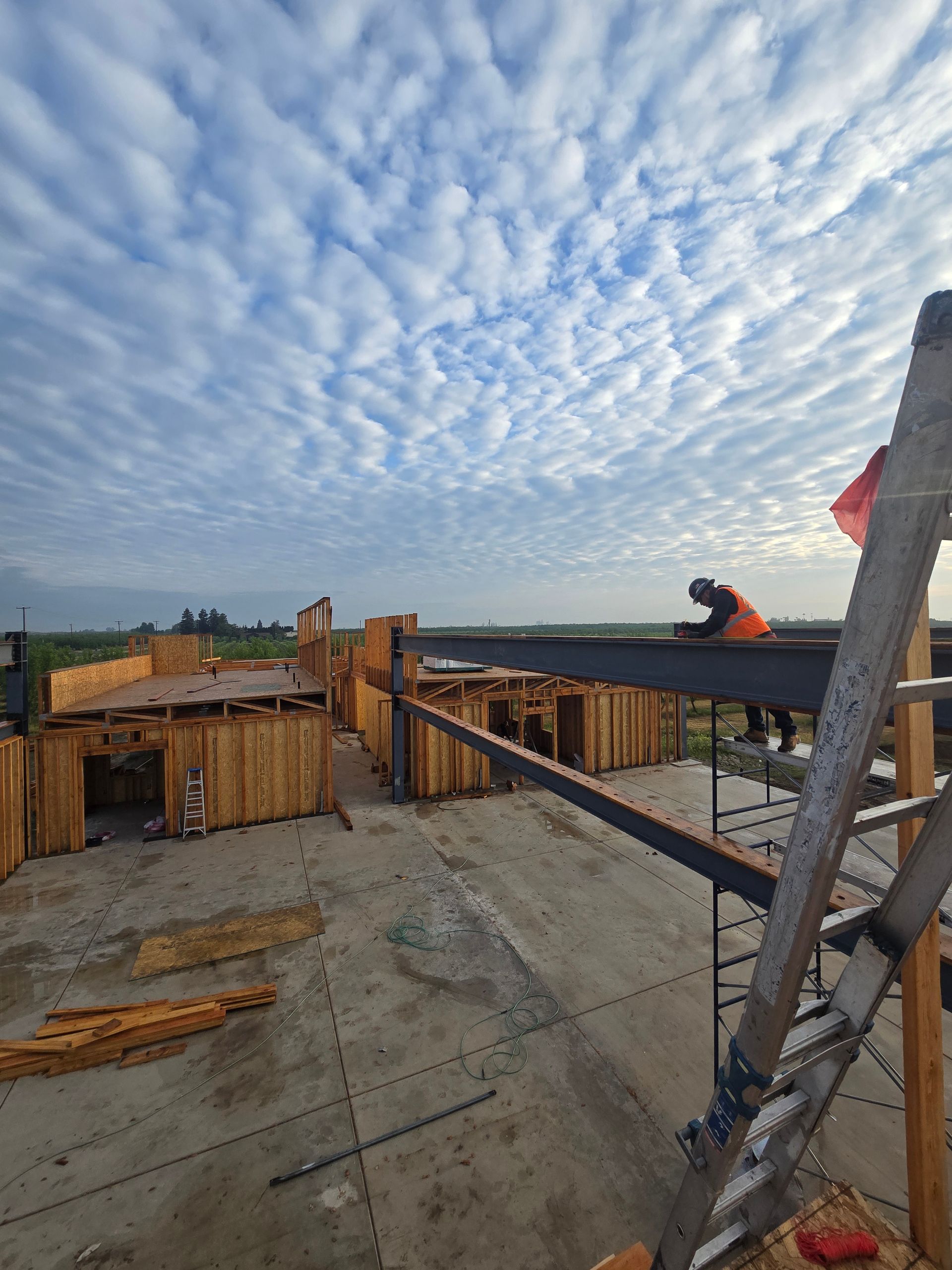 Construction site rooftop with workers, wooden formwork, and a cloudy sky at dawn or dusk