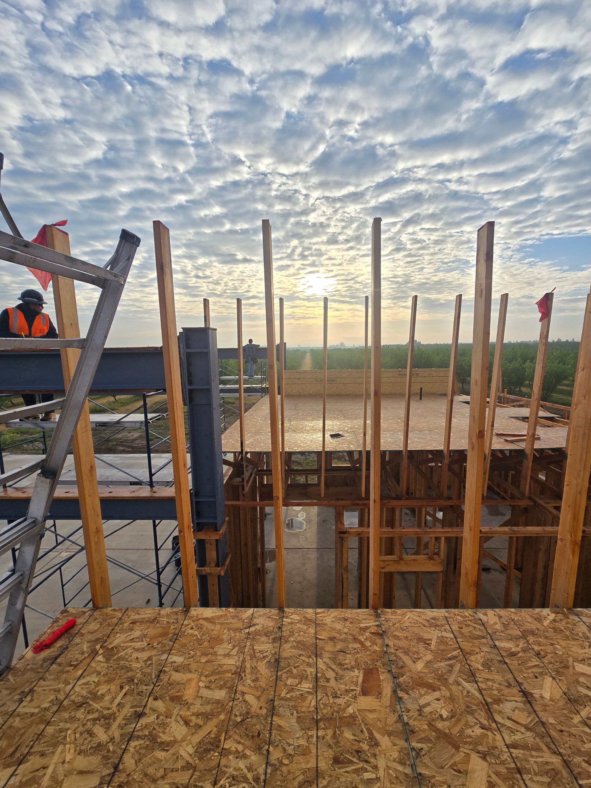 Construction site with wooden framing and workers under a cloudy sky at sunrise