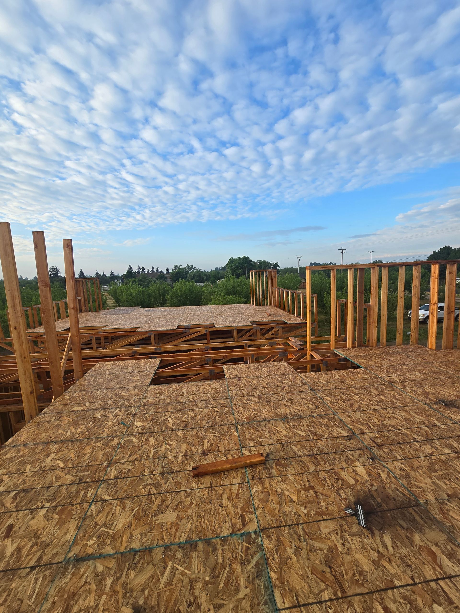 Wooden foundation posts and beams on a construction site under a blue, cloud-filled sky