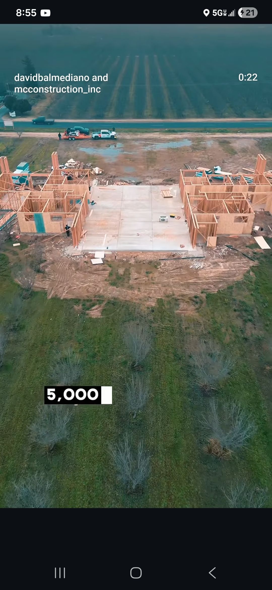 Aerial view of a rural site with earthworks, two buildings, and a cleared central area near a body of water.