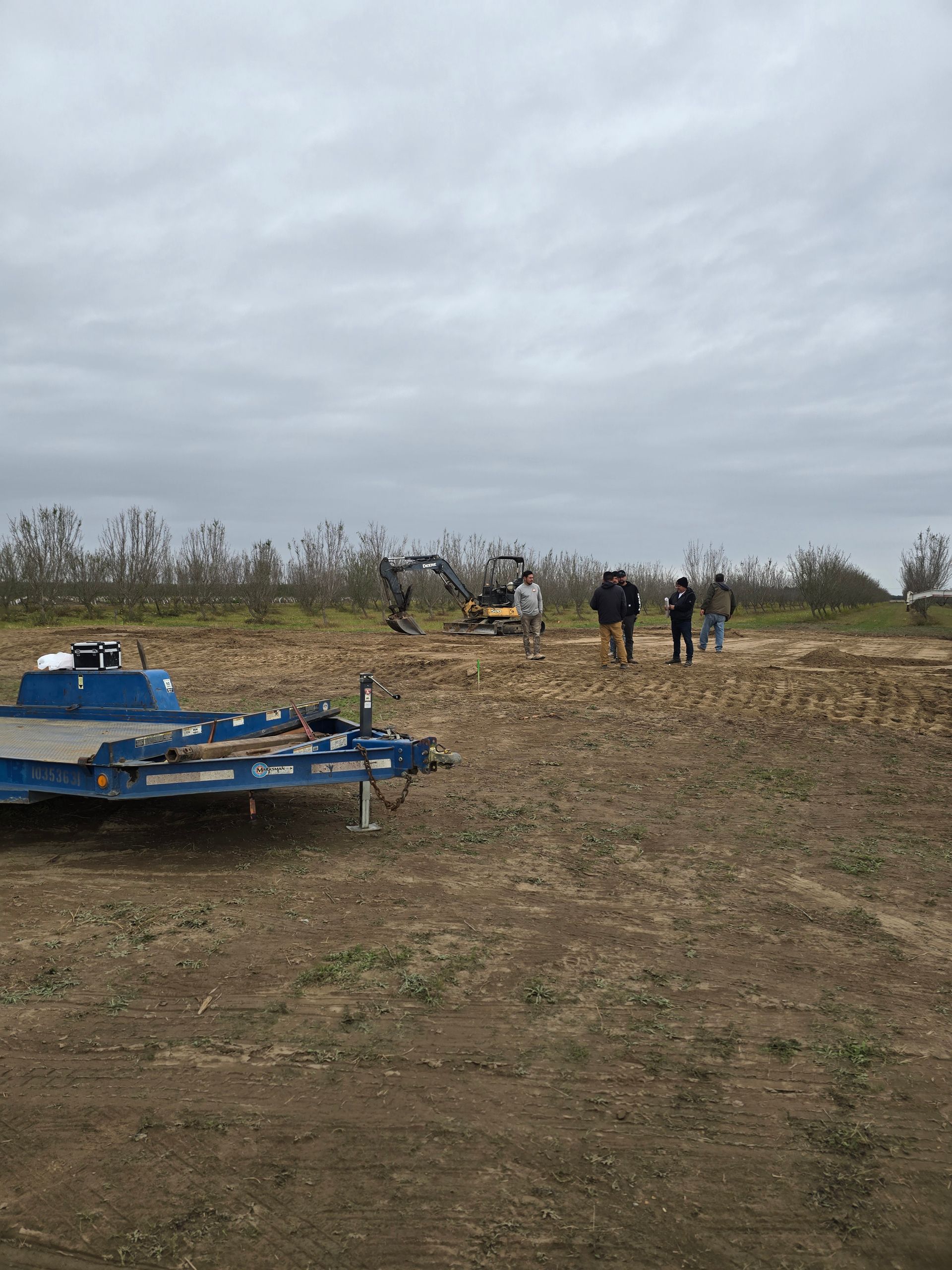 People standing near blue farm equipment in a muddy field under a cloudy sky