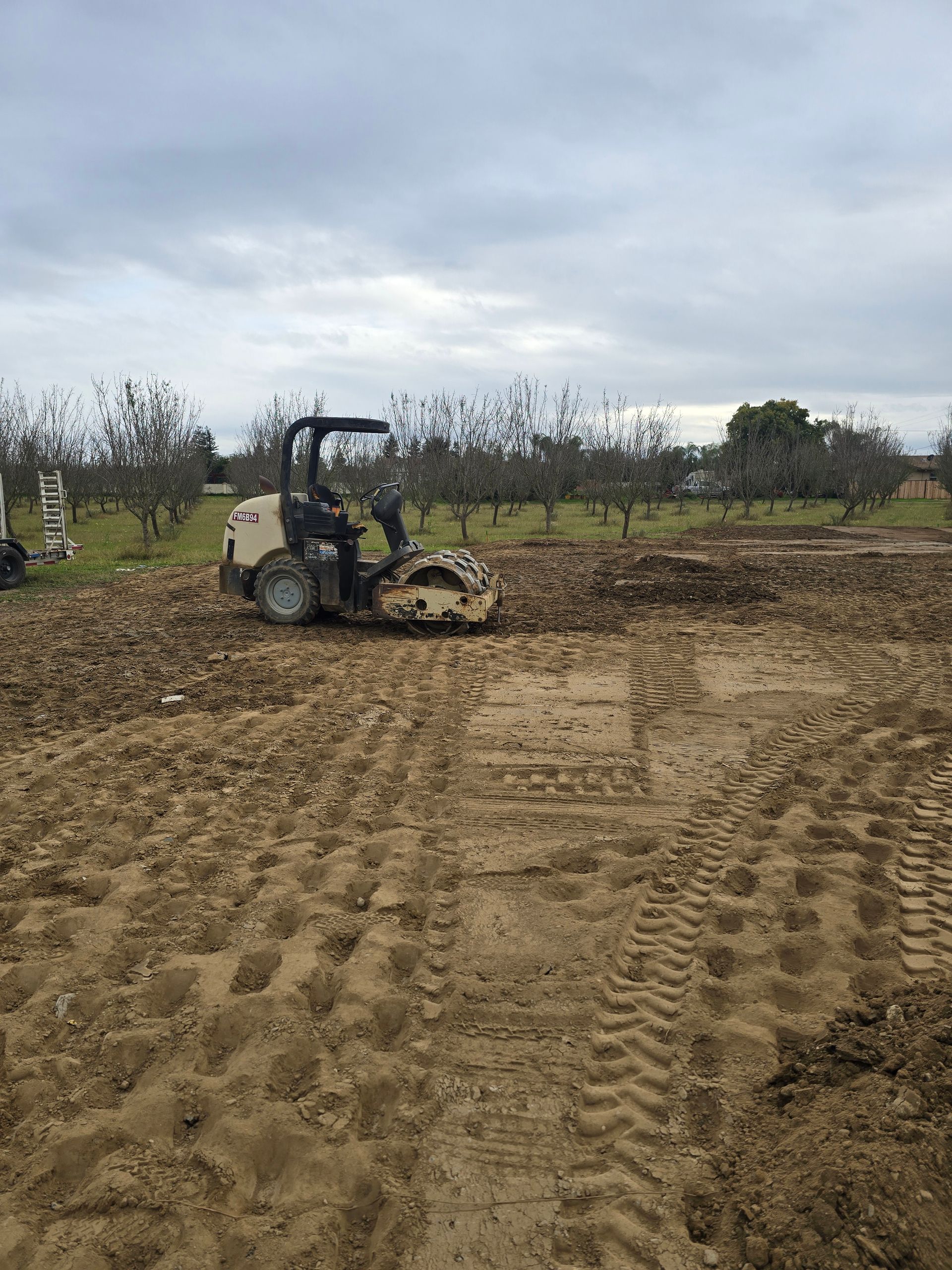 Tractor grading a dirt field under a cloudy sky, with tire tracks in the foreground.