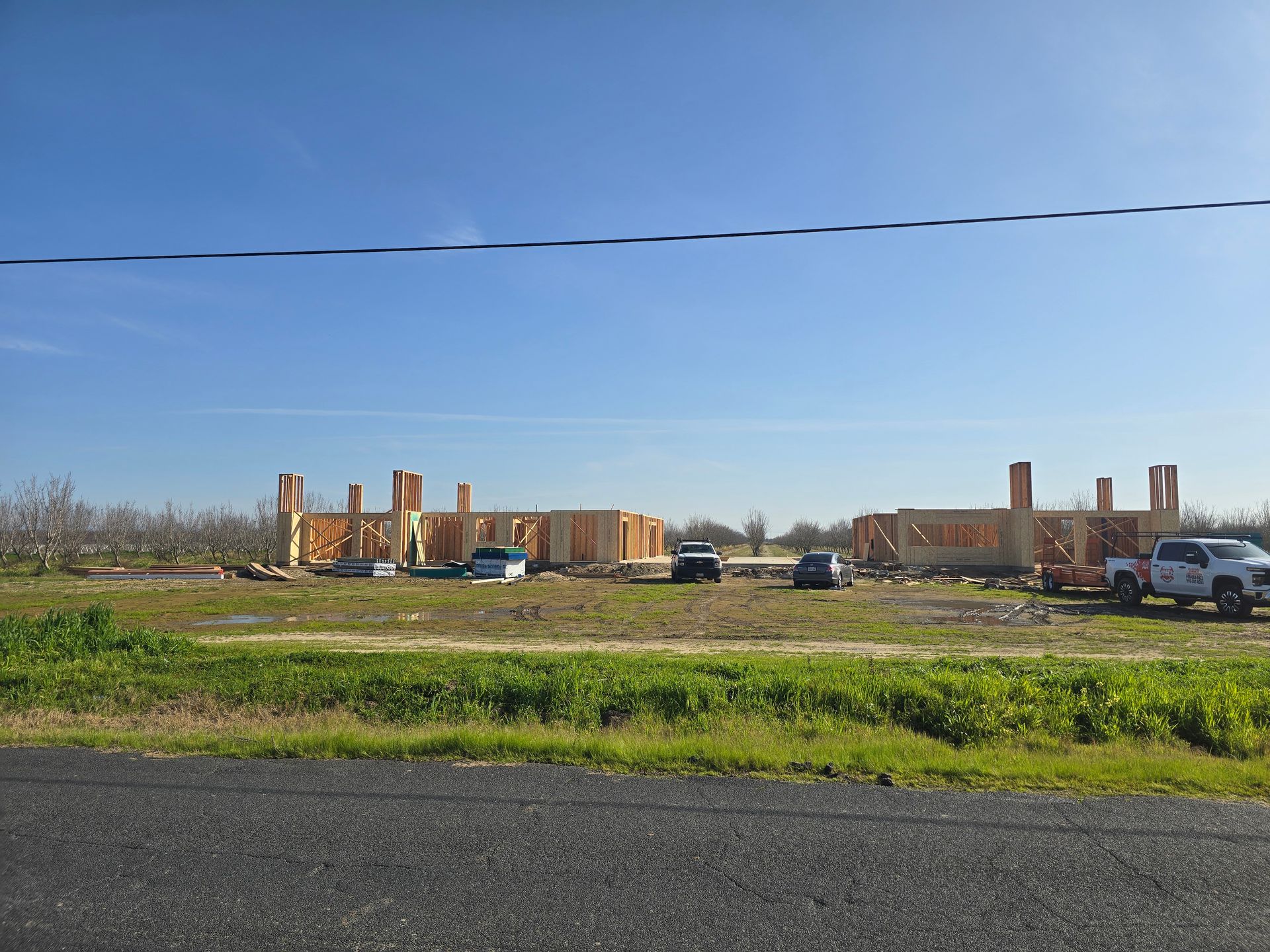 Wide field with brick buildings under construction, parked trucks, and a clear blue sky.