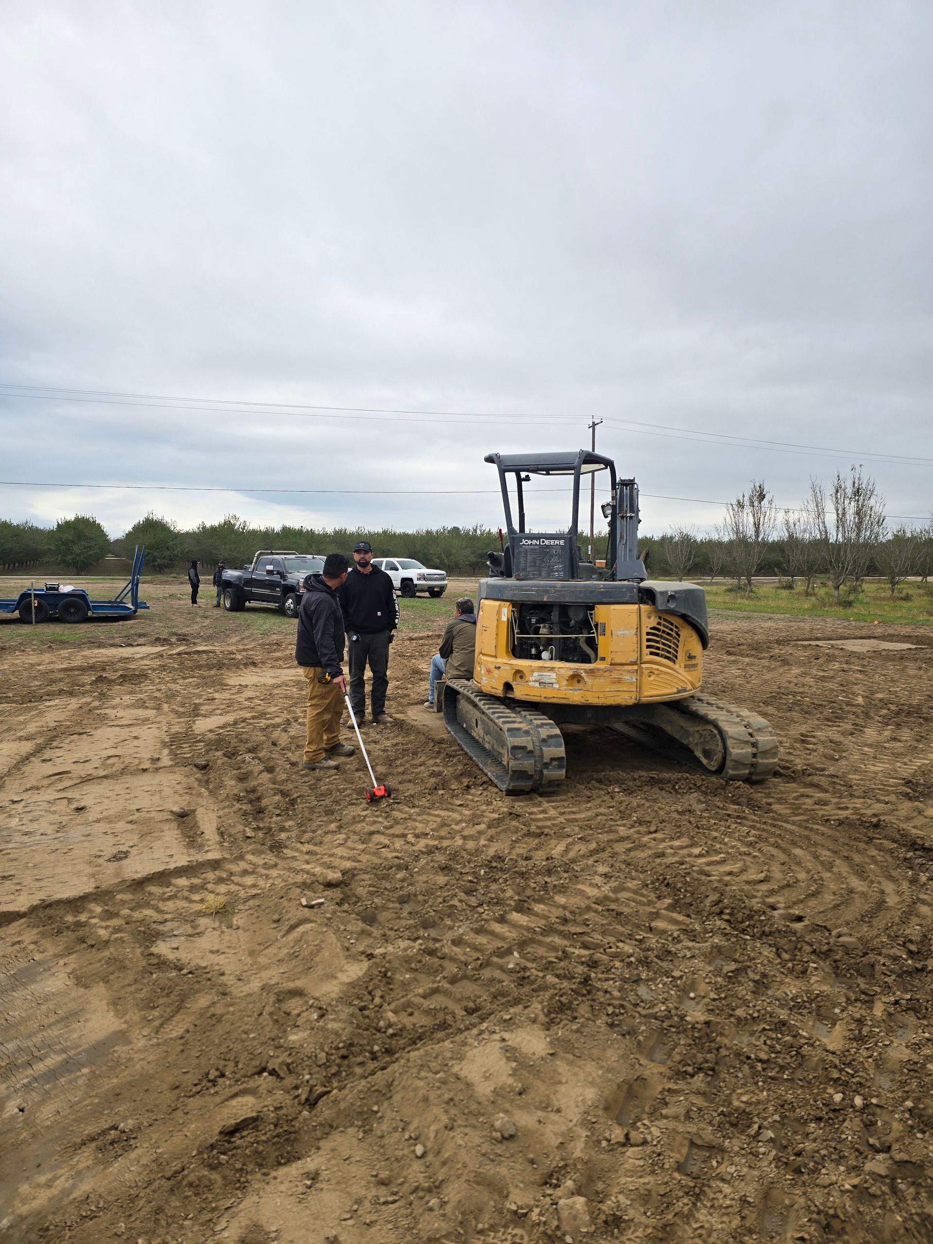 Yellow bulldozer on muddy construction site with two people standing nearby under cloudy sky