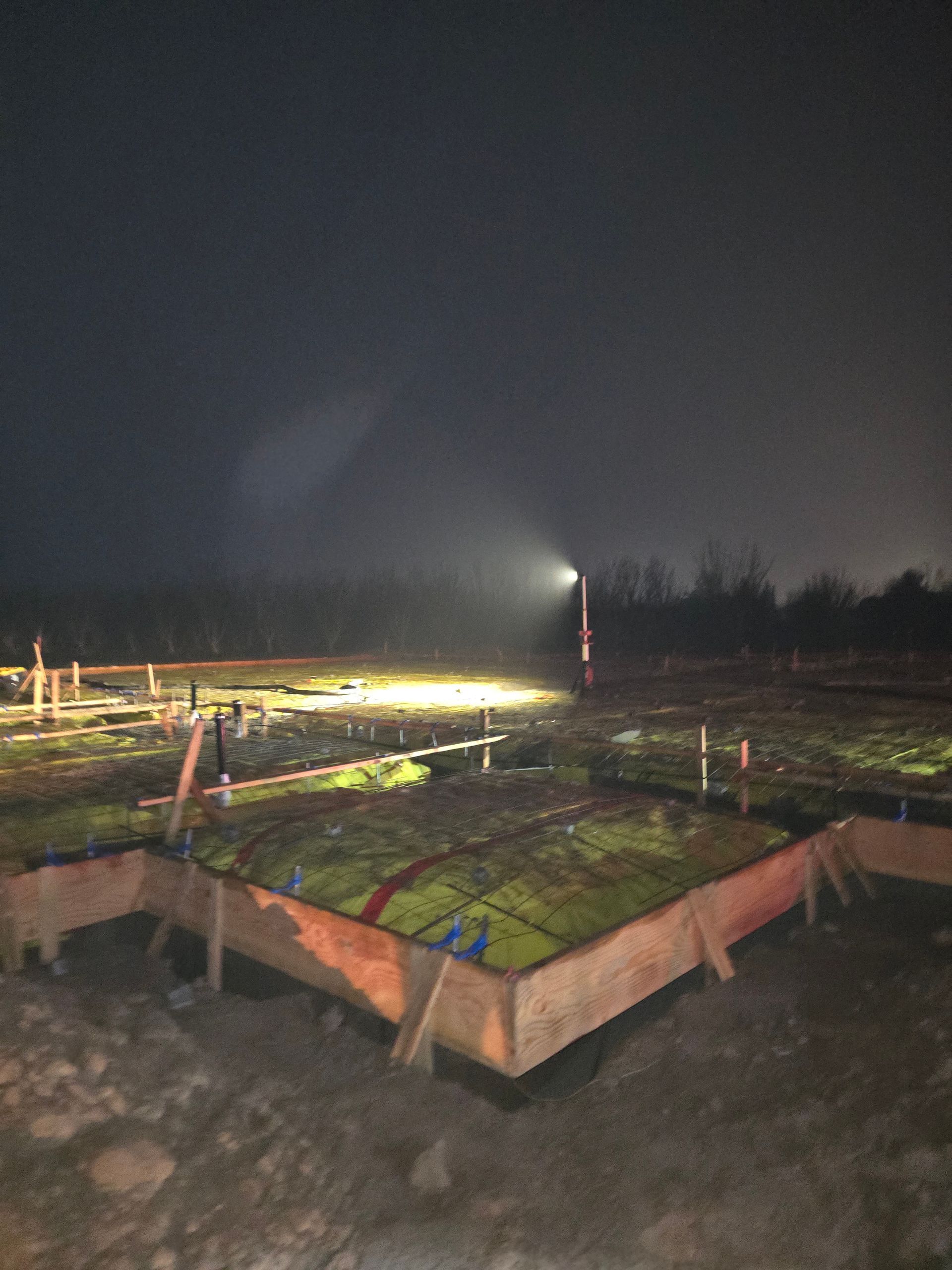 Nighttime field with a lit irrigation sprinkler spraying water over rows of green crops