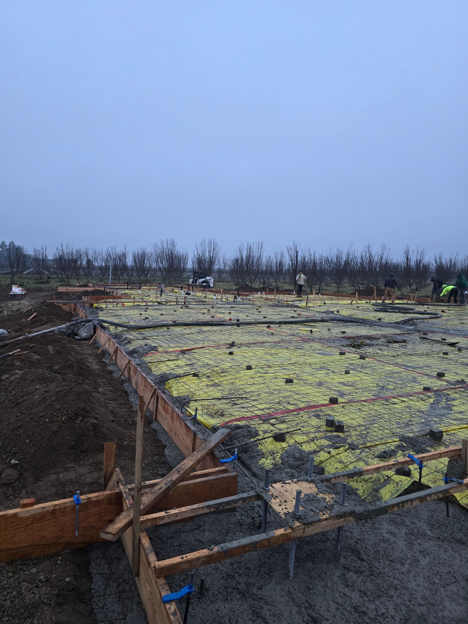 Concrete foundation slab under construction with wooden forms and muddy ground on an overcast day