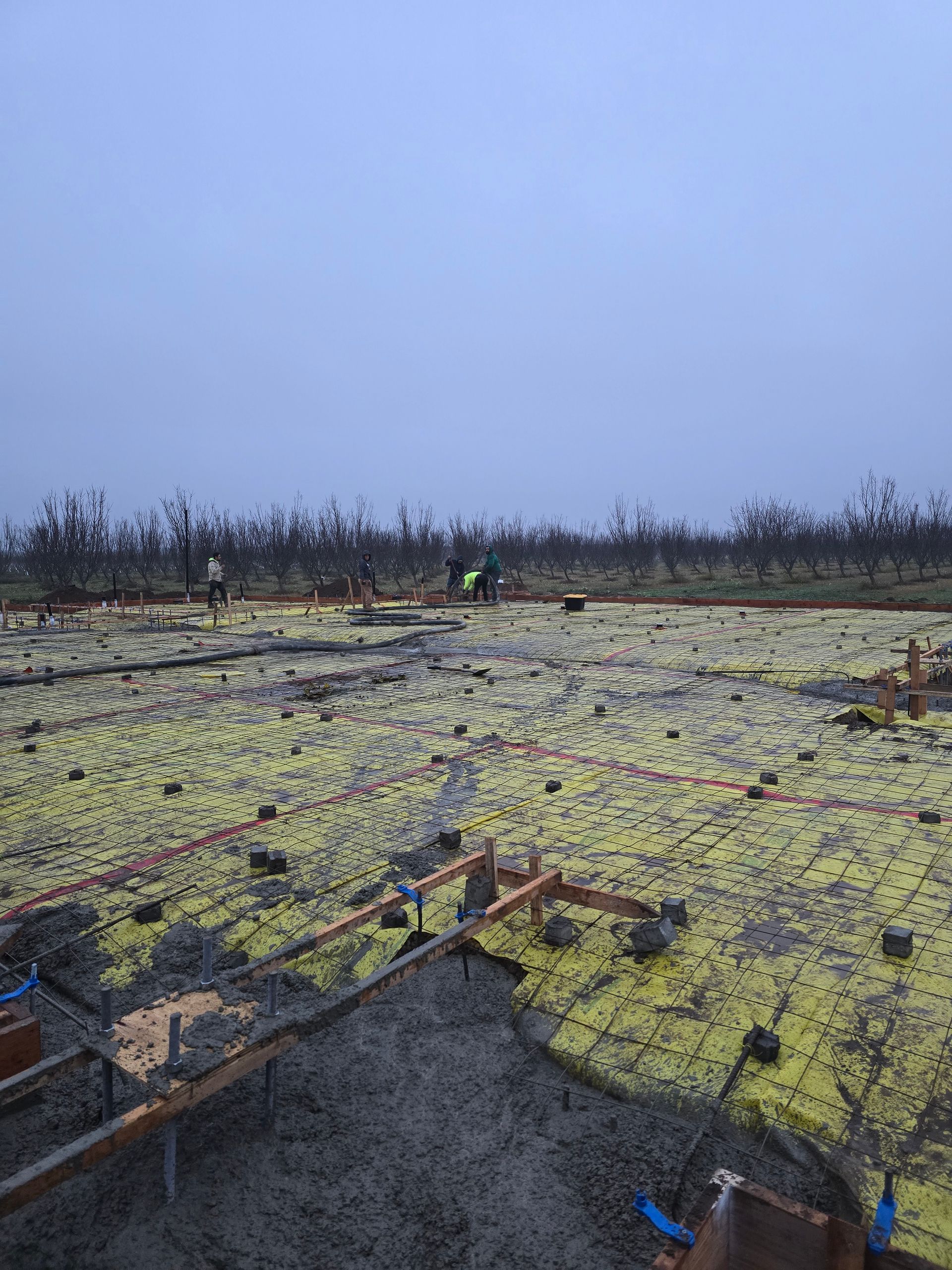 Workers on a rooftop covered with yellow insulation, with tools and materials scattered under a gray sky