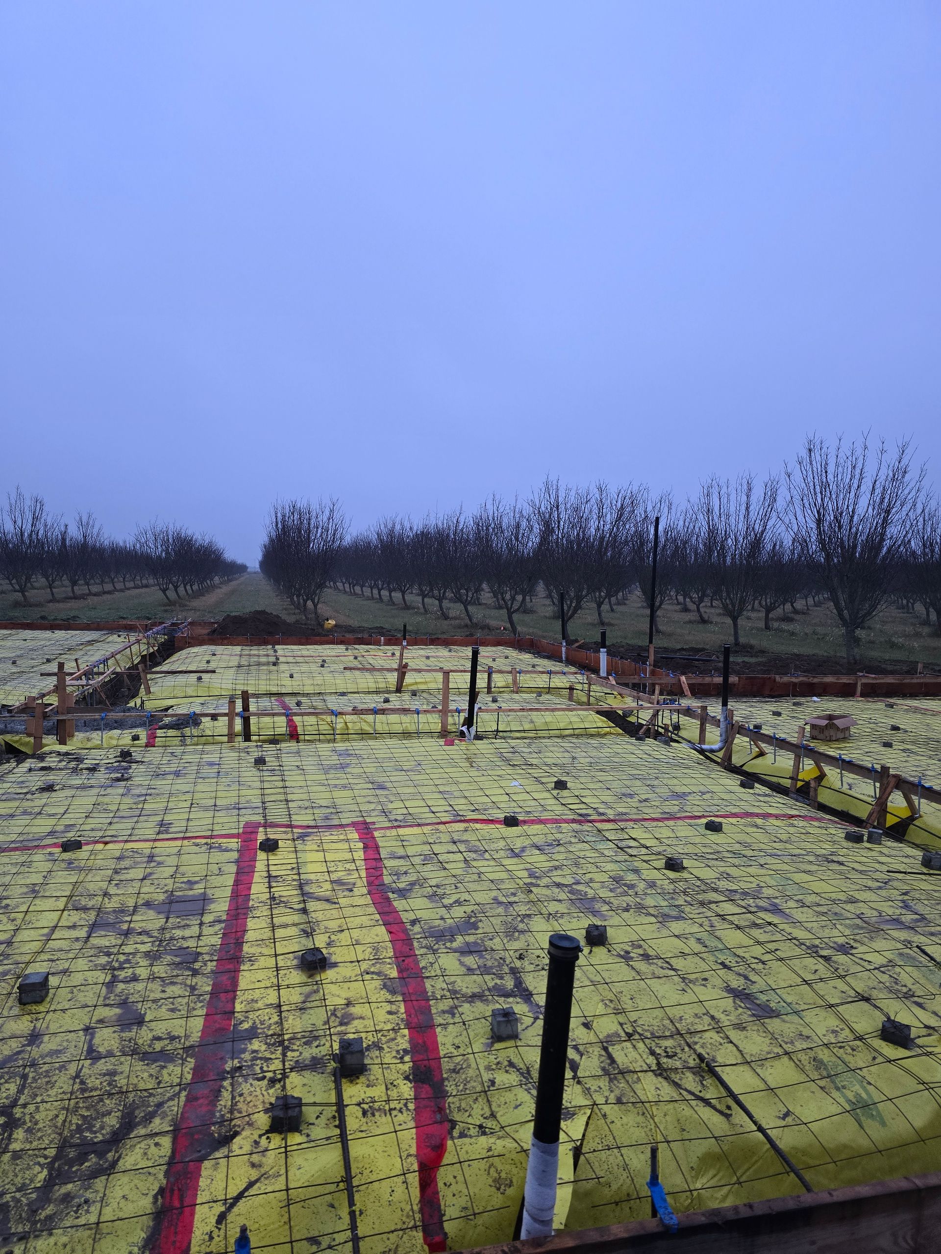 Yellow-covered rooftop with red stripes and pipes under a cloudy sky, overlooking trees in the distance